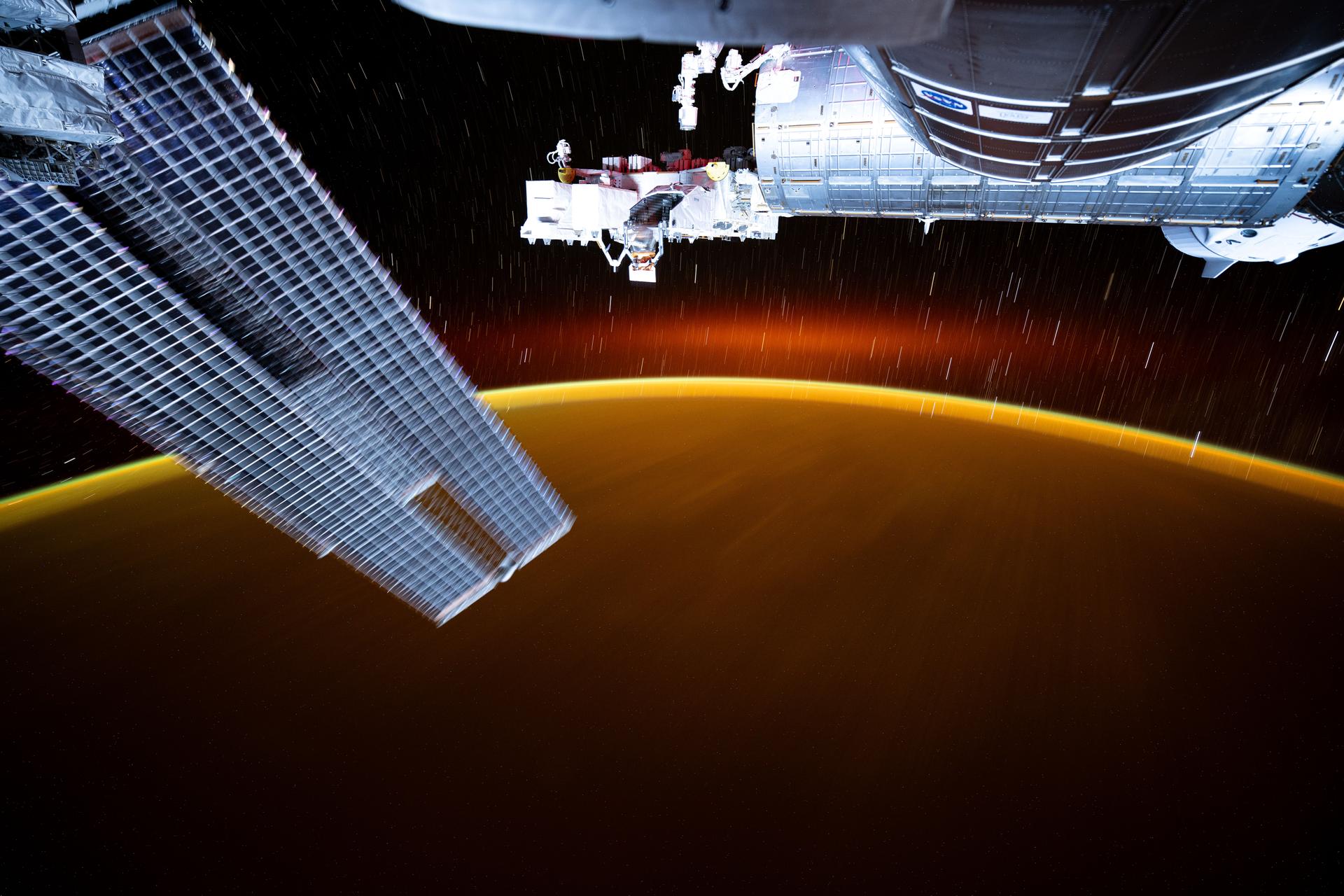 This long-duration photograph from the International Space Station highlights star trails and an atmospheric glow blanketing Earth's horizon. In the foreground, is a set of the space station's main solar arrays (left), the Kibo laboratory module (right), and Kibo's External Platform that houses experiments exposed to the vacuum of space. The orbital outpost was soaring 259 miles above the Pacific Ocean southeast of Japan going into a sunset.