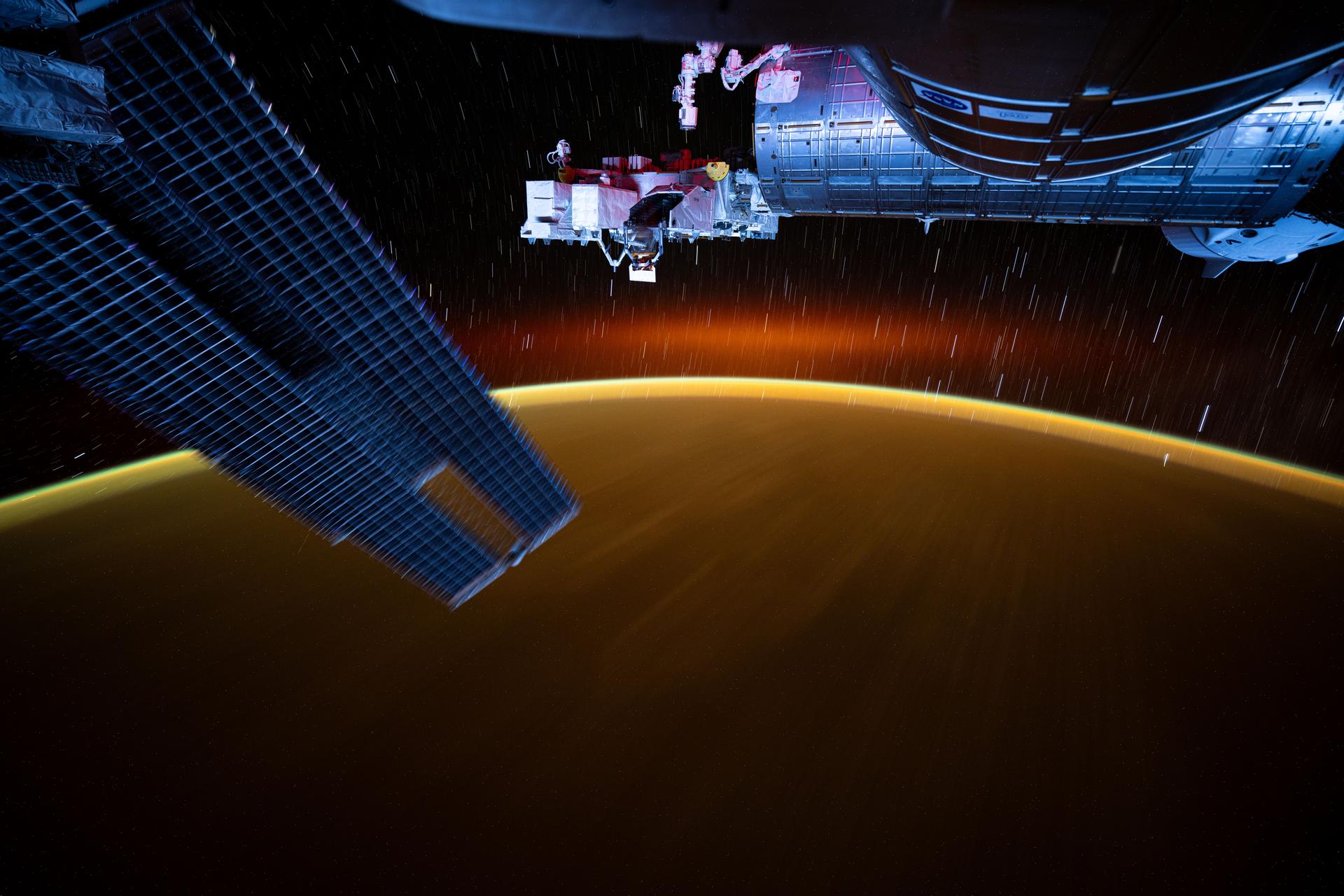 This long-duration photograph from the International Space Station highlights star trails and an atmospheric glow blanketing Earth's horizon. In the foreground, is a set of the space station's main solar arrays (left), the Kibo laboratory module (right), and Kibo's External Platform that houses experiments exposed to the vacuum of space. The orbital outpost was soaring 259 miles above the Pacific Ocean southeast of Japan just after sunset.