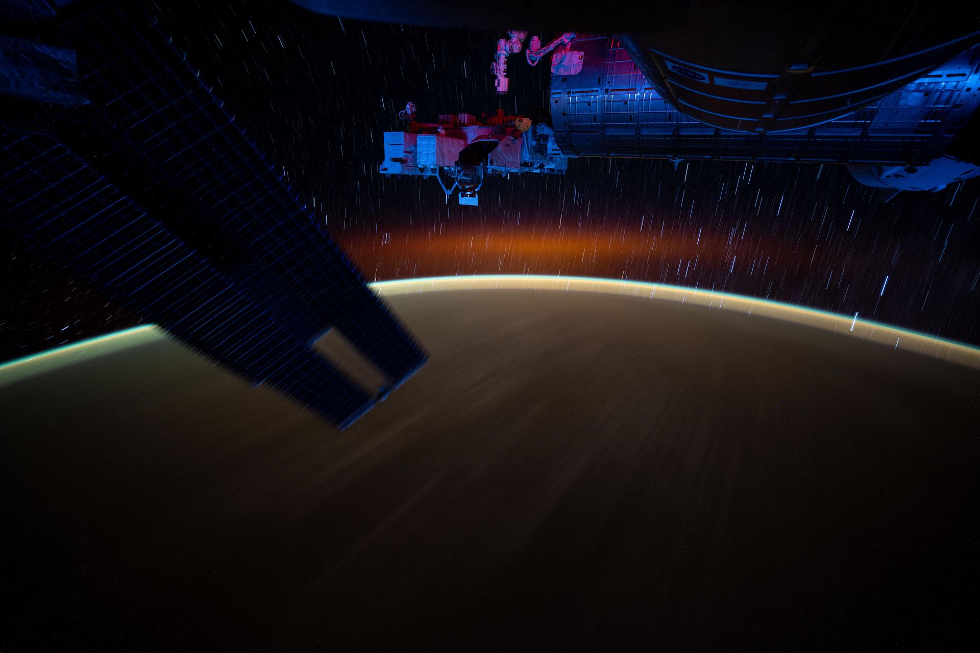 This long-duration photograph from the International Space Station highlights star trails and an atmospheric glow blanketing Earth's horizon. In the foreground, is a set of the space station's main solar arrays (left), the Kibo laboratory module (right), and Kibo's External Platform that houses experiments exposed to the vacuum of space. The orbital outpost was soaring 259 miles above the Pacific Ocean southeast of Japan after sunset.