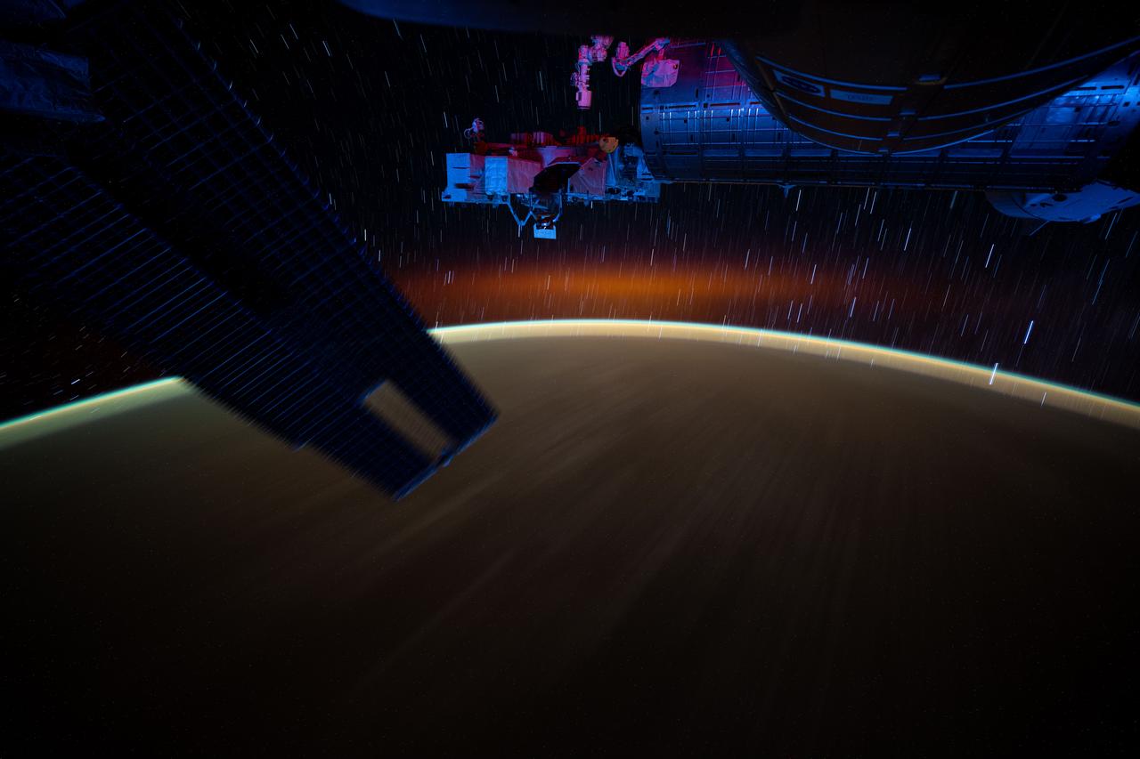 iss072e921629 (March 30, 2025) --- This long-duration photograph from the International Space Station highlights star trails and an atmospheric glow blanketing Earth's horizon. In the foreground, is a set of the space station's main solar arrays (left), the Kibo laboratory module (right), and Kibo's External Platform that houses experiments exposed to the vacuum of space. The orbital outpost was soaring 259 miles above the Pacific Ocean southeast of Japan after sunset.