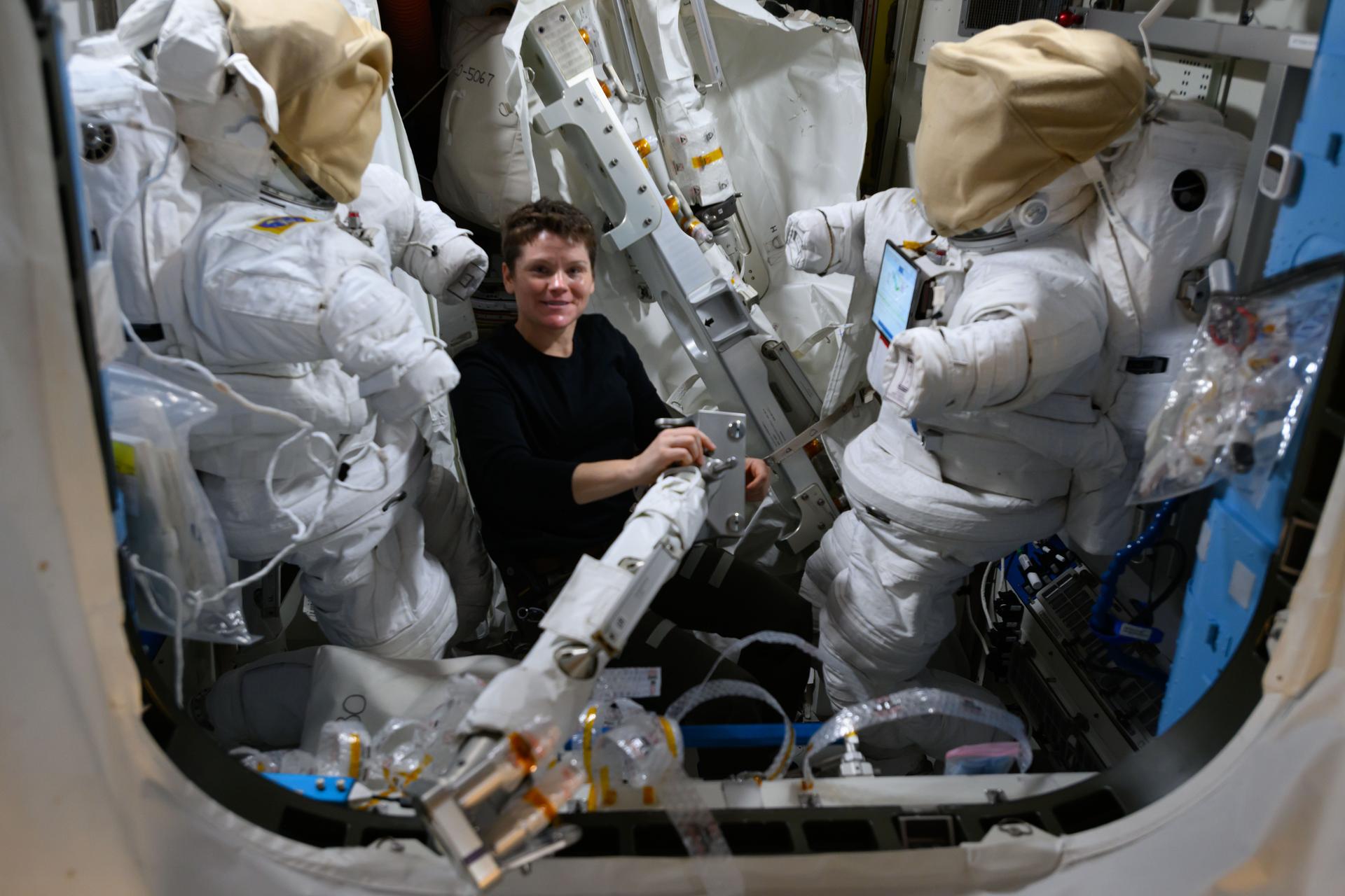 NASA astronaut and Expedition 72 Flight Engineer Anne McClain works inside the Quest airlock assembling hardware that will be installed during an upcoming spacewalk to prepare the International Space Station for a new rollout solar array. On either side of McClain, are two spacesuits staged inside Quest being readied for the maintenance spacewalk.