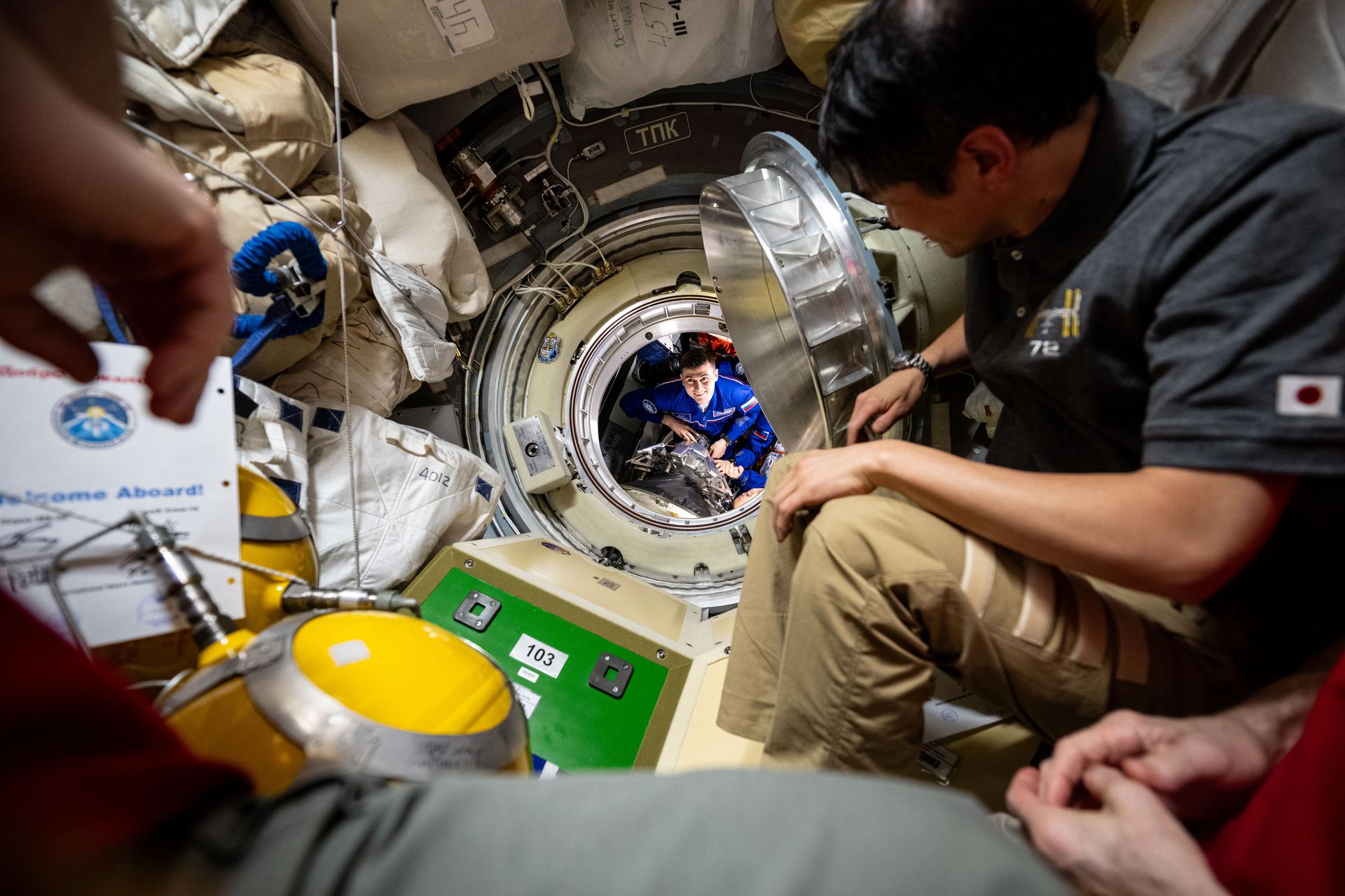 Roscosmos cosmonaut and Expedition 72 Flight Engineer Alexey Zubritsky is pictured before entering the International Space Station shortly after docking to the Prichal module aboard the Soyuz MS-27 spacecraft. Waiting to greet Zubritsky is Flight Engineer Takuya Onishi of JAXA (Japan Aerospace Exploration Agency), at right.
