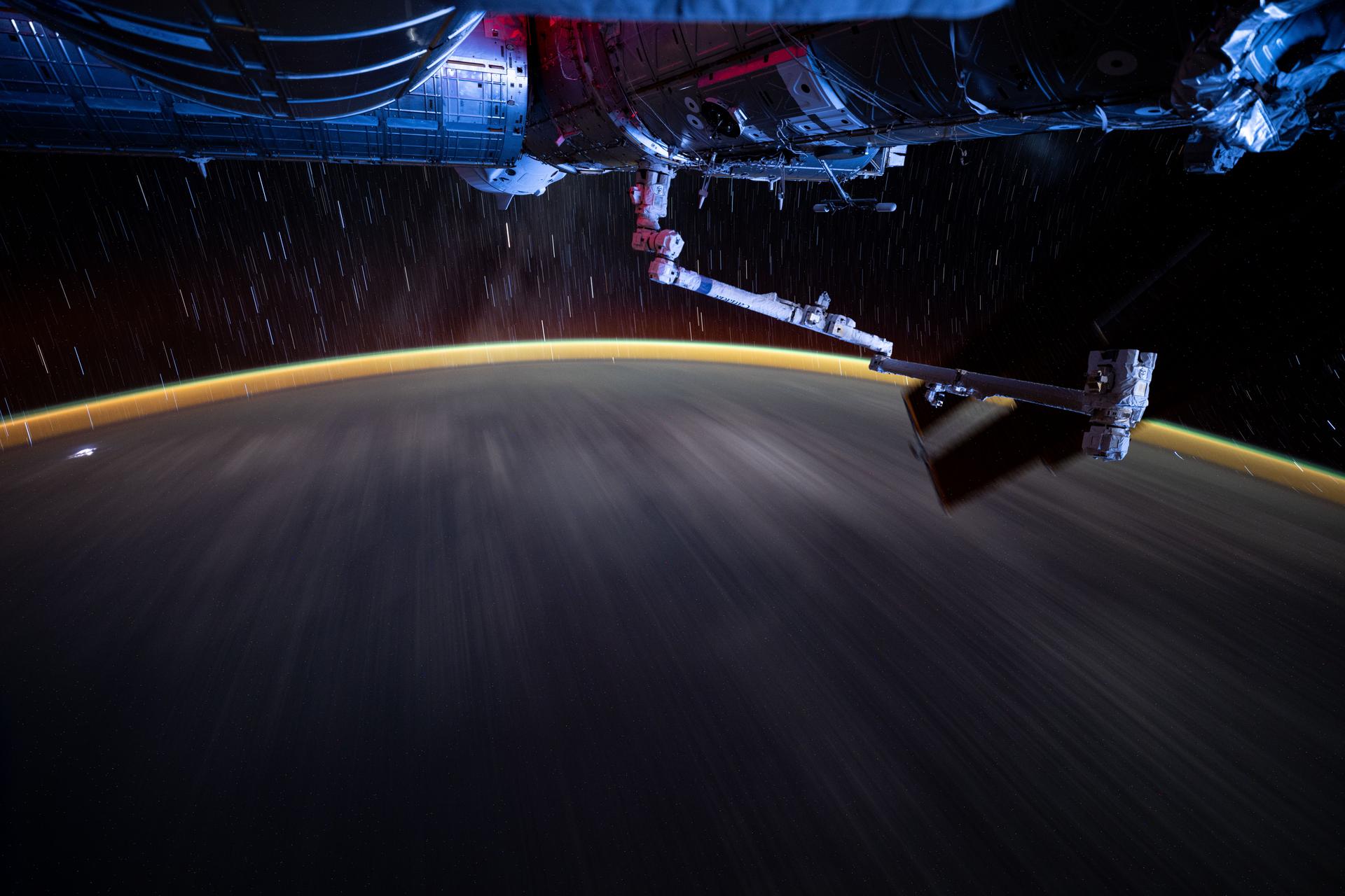 This long duration photograph reveals Earth's atmopsheric glow underneath star trails as the International Space Station orbited 258 miles above the Pacific Ocean southeast of Hawaii at approximately 8:16 p.m. local time. In the foreground (from left), is the Kibo laboratory module, the partially obscured SpaceX Dragon crew spacecraft docked to the Harmony module, the Canadarm2 robotic arm, and the Destiny laboratory module.