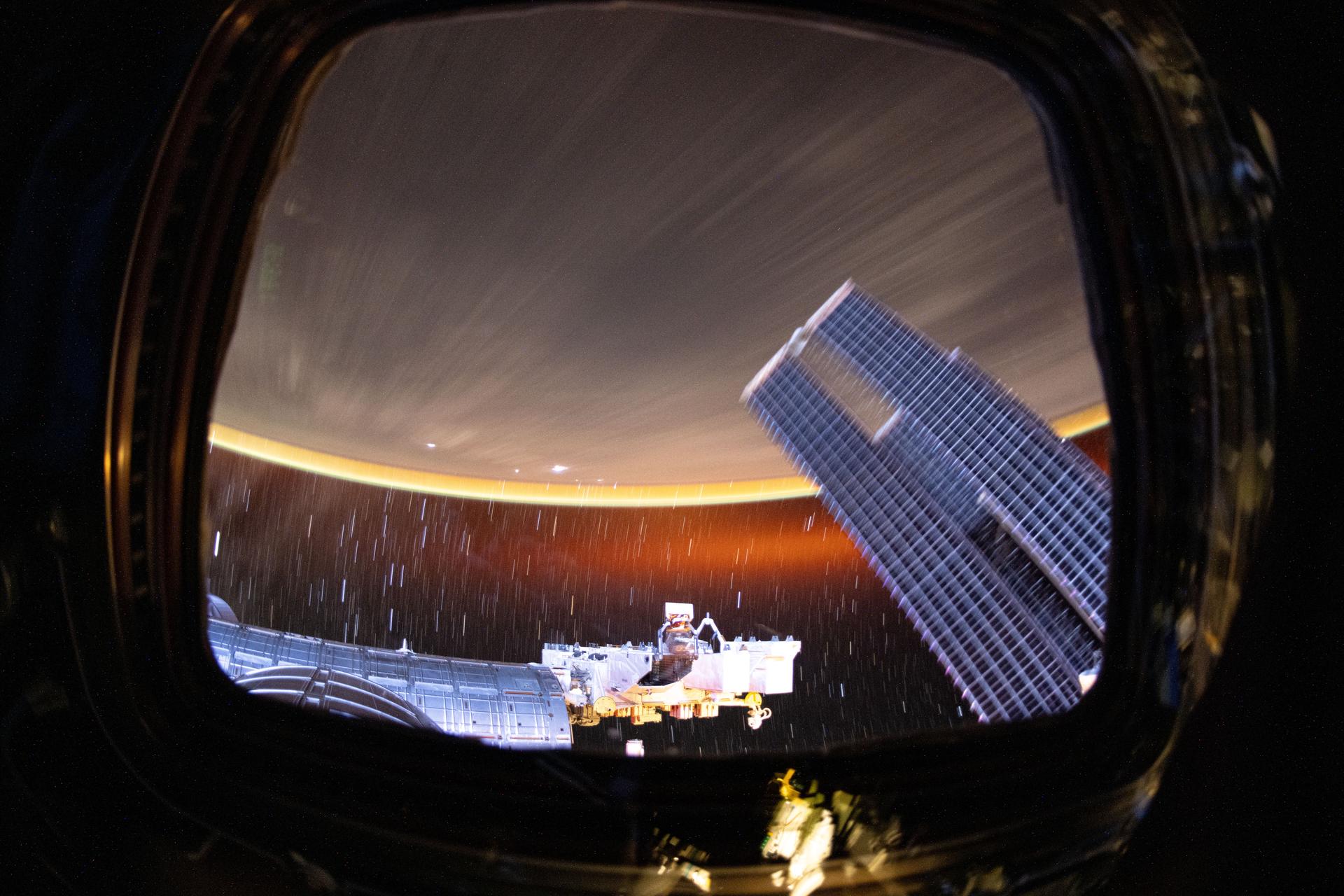 This long duration photograph looks out from a window on the cupola revealing Earth's atmopsheric glow underneath star trails as the International Space Station orbited 258 miles above the Pacific Ocean southeast of Hawaii at approximately 8:15 p.m. local time. In the foreground, is the Kibo laboratory module (left), and Kibo's External Platform (center) that houses experiments exposed to the vacuum of space, and a set of the space station's main solar arrays (right).
