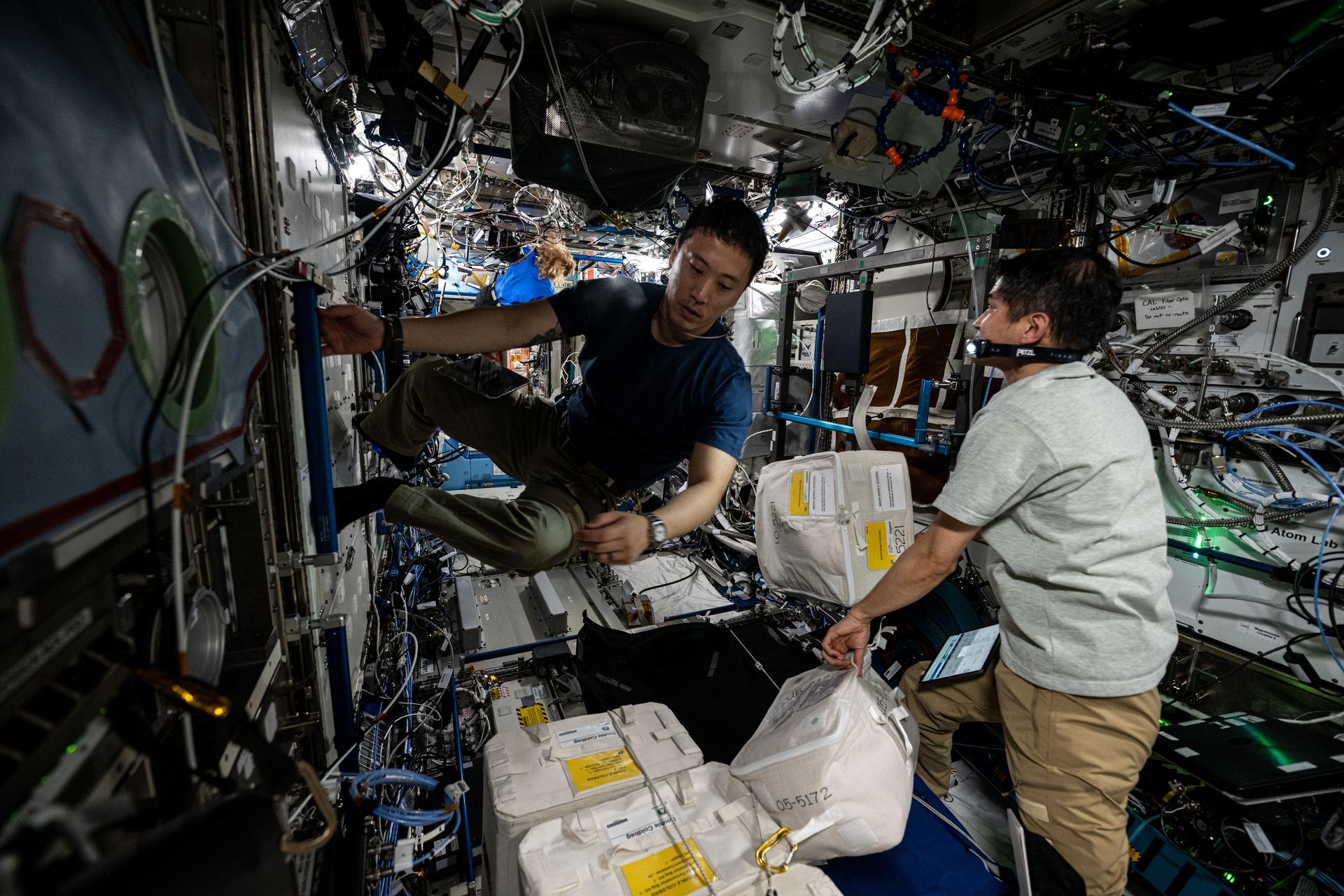 (From left) Astronauts Jonny Kim of NASA and Takuya Onishi of JAXA (Japan Aerospace Exploration Agency), Expedition 73 Flight Engineer and Commander respectively, work inside the International Space Station's Destiny laboratory module stowing cargo recently delivered aboard the SpaceX Dragon cargo craft.