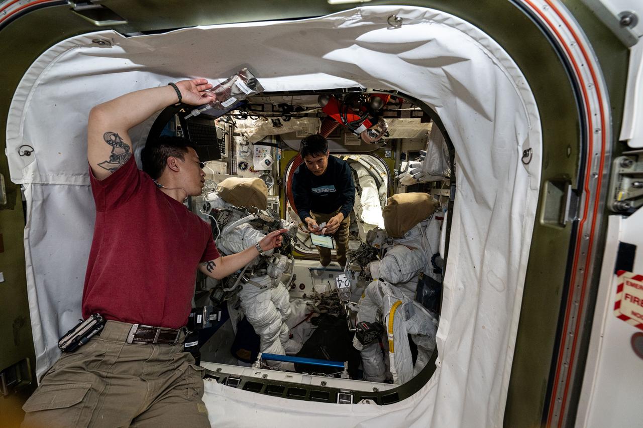 iss073e0003041 (May 10, 2025) --- (From left) Astronauts Jonny Kim of NASA and Takuya Onishi of JAXA (Japan Aerospace Exploration Agency), Expedition 73 flight engineer and commander respectively, work inside the International Space Station's Quest airlock setting up a pair of spacesuits. Expedition 73 Flight Engineers Anne McClain and Nichole Ayers (both out of frame), both from NASA, would wear the suits the following day during a spacewalk to upgrade the orbital outpost's power generation system and relocate a communications antenna.