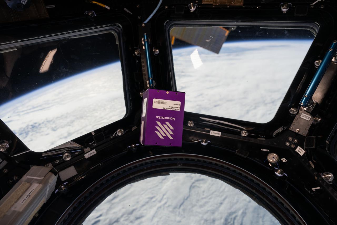 iss073e0025760 (5/8/2025) ---  NanoRacks Module-48, S/N 1009 floats in front of the windows in the Cupola module aboard the International Space Station as part of the NanoRacks-Lagrange investigation. The module holds student photos, printed logos sheets, and plant seeds and is launched to the space station with a message card. The students plant the seeds once they return to Earth and compare them to plants grown from regular seeds. This investigation seeks to increase interest in space.