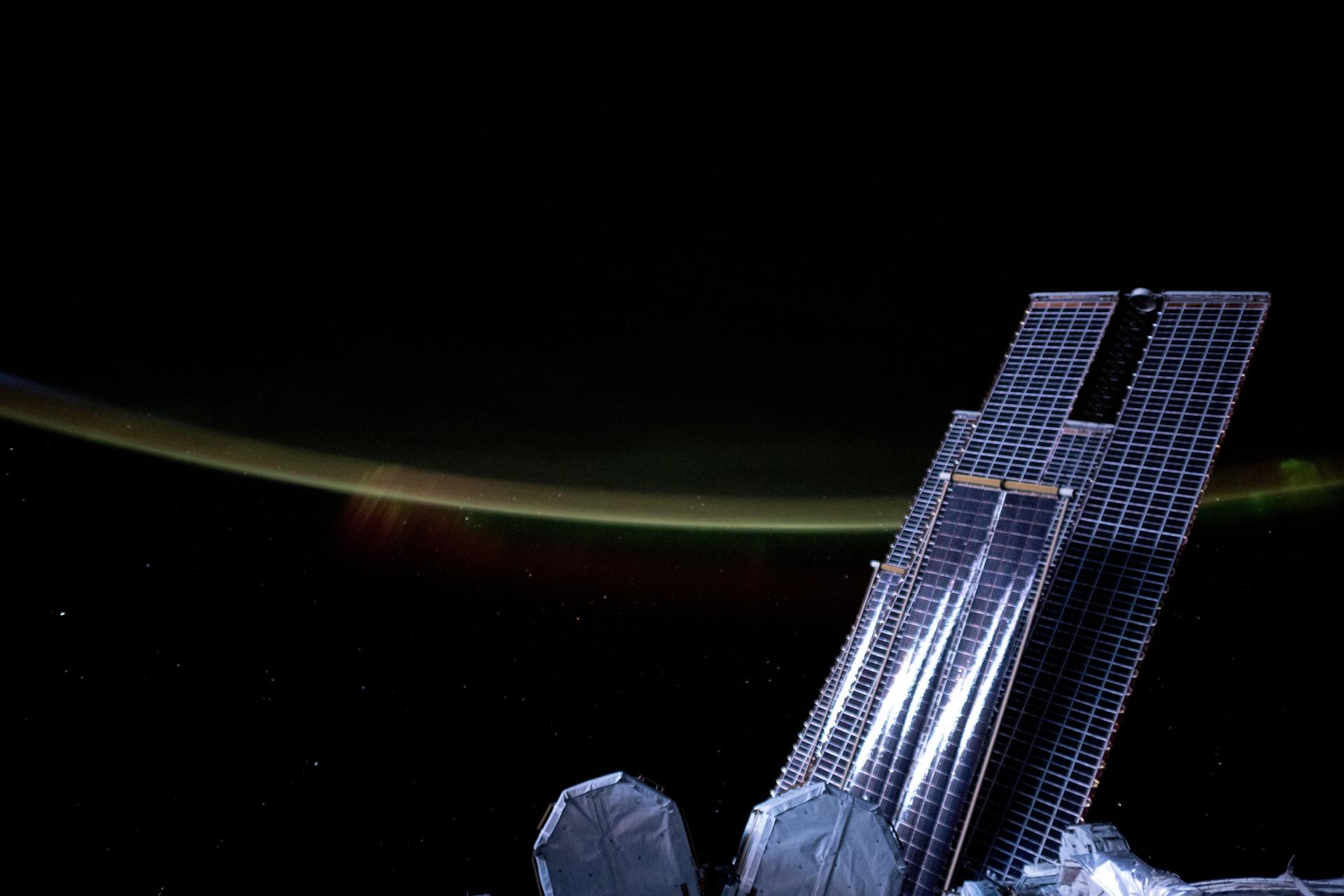 Moonlight casts a silvery light on a set of the International Space Station's main solar arrays and rollout solar arrays and crowned by Earth's atmospheric glow and a wispy aurora as it orbited 272 miles above the southern Indian Ocean at approximately 8:06 p.m. local time.