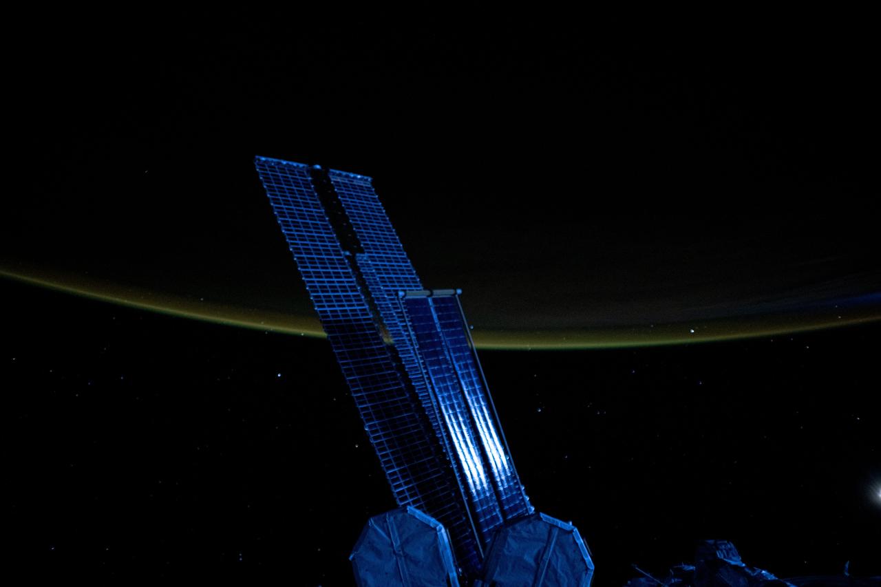 iss073e0041283 (April 23, 2025) --- Moonlight casts a blue light on a set of the International Space Station's main solar arrays and rollout solar arrays and crowned by Earth's atmospheric glow as it orbited 259 miles above the North Pacific Ocean at approximately 3:39 a.m. local time.
