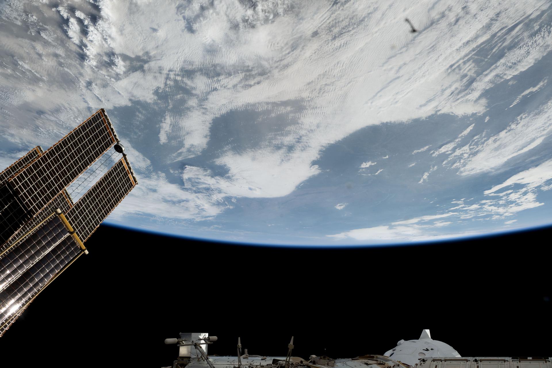 Partially obscured, at bottom right, is the SpaceX Dragon crew spacecraft docked to the Harmony module's forward port on the International Space Station. At left, are a set of the orbital outpost's main solar arrays and rollout solar arrays. The space station was orbiting 262 miles above a cloudy North America at the time of this photograph.