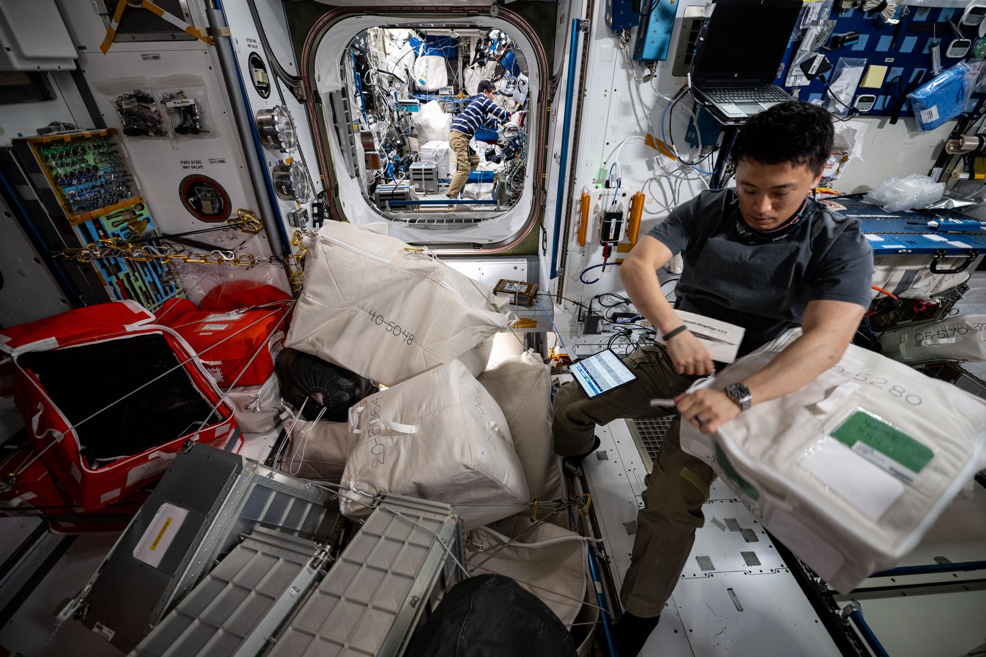 NASA astronaut and Expedition 73 Flight Engineer Jonny Kim works inside the International Space Station's Harmony module gathering and organizing cargo to be packed inside the SpaceX Dragon cargo spacecraft before its departure. In the rear, station Commander Takuya Onishi from JAXA (Japan Aerospace Exploration Agency) works inside the Columbus laboratory module.