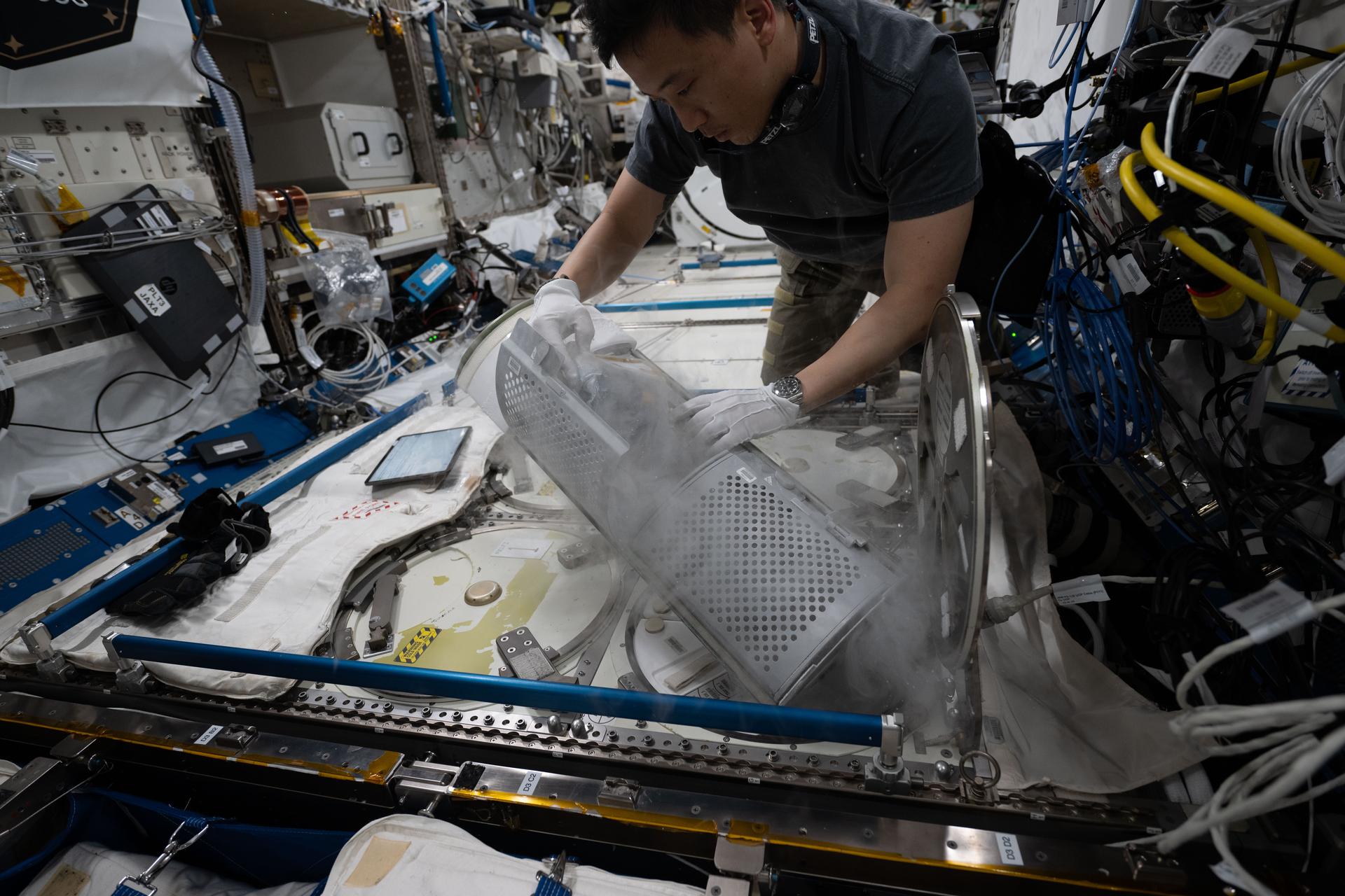 NASA astronaut and Expedition 73 Flight Engineer Jonny Kim removes a cryogenic storage unit, called a dewar, containing frozen protein crystal samples from a science freezer located inside International Space Station's Kibo laboratory module. The research activities were part of a technology demonstration potentially enabling the synthesis of medications during deep space missions and improving the pharmaceutical industry on Earth.