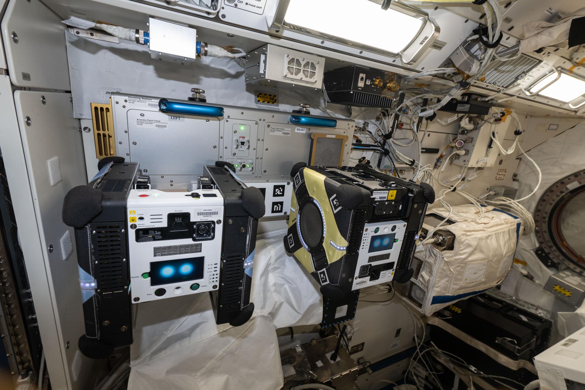 A pair of Astrobee robotic free-flyers are pictured docked to ports inside the International Space Station's Kibo laboratory module. The cube-shaped, toaster-sized robots are being tested for their ability to autonomously navigate aboard the orbital outpost and conduct routine maintenance and monitoring duties enabling the crew to focus on science and engineering duties.