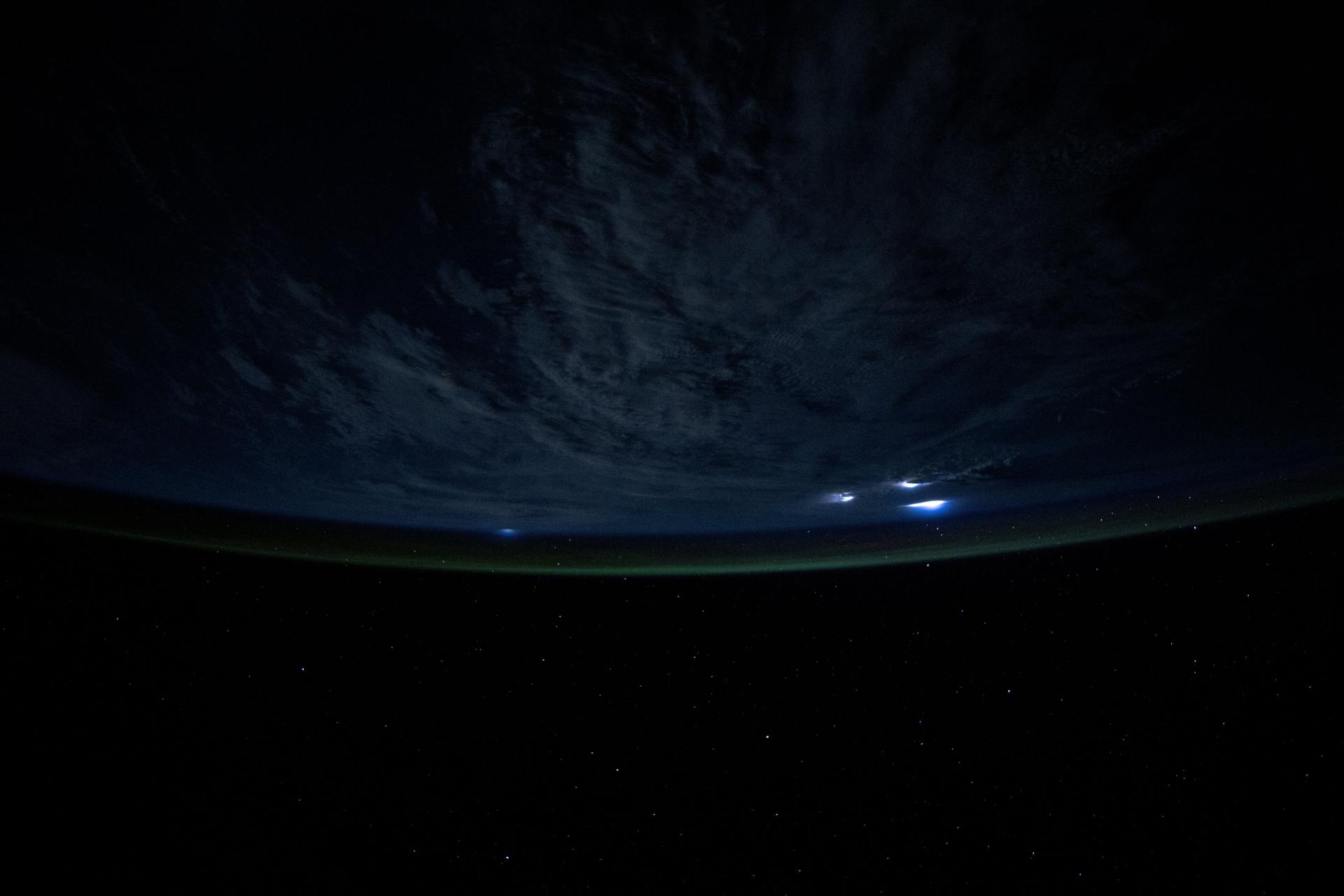 Lightining illuminates the cloud tops during a storm underneath Earth's atmospheric glow in this photograph from the International Space Station as it orbited 259 miles above the Atlantic Ocean east of the Bahamas.