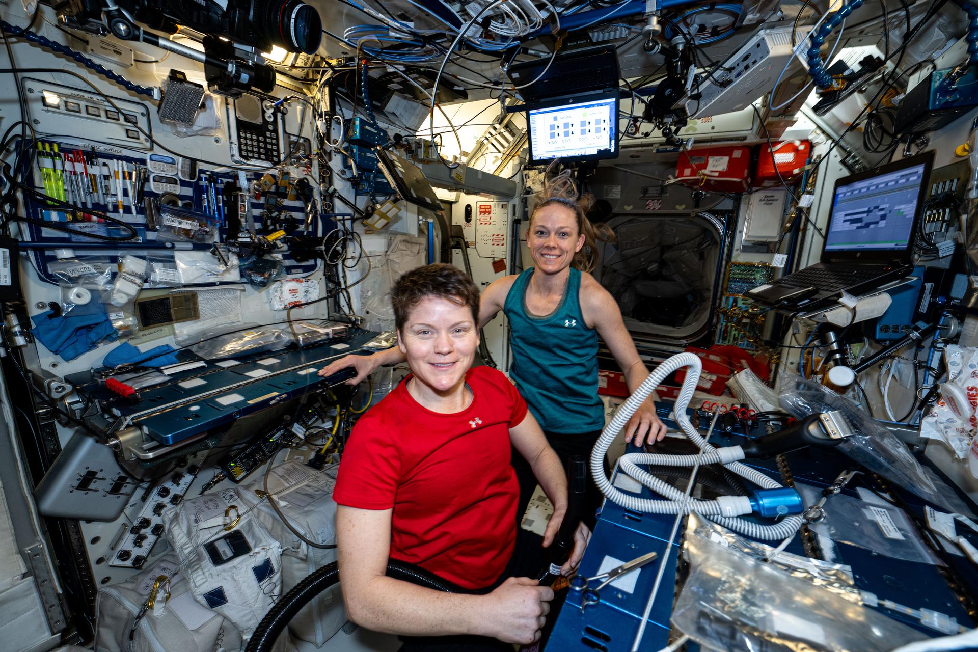 NASA astronauts (left to right) Anne McClain and Nichole Ayers, both Expedition 73 Flight Engineers, pose for a portrait together aboard the International Space Station's Harmony module. Moments earlier, Ayers finished trimming McClain's hair using an electric razor with a suction hose attached that collects the loose hair to protect the station's atmosphere.