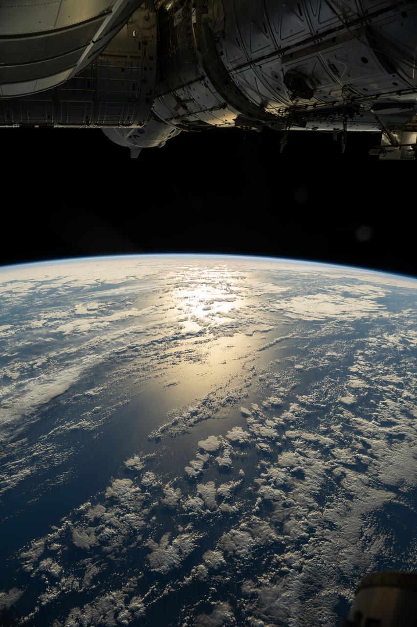 iss073e0177079 (June 2, 2025) --- The sun's glint beams off a partly cloudy southern Pacific Ocean in this photograph from the International Space Station as it orbited 264 miles above. At top, a partially obscured SpaceX Dragon crew spacecraft can be seen docked to the orbital outpost's forward port on the Harmony module.