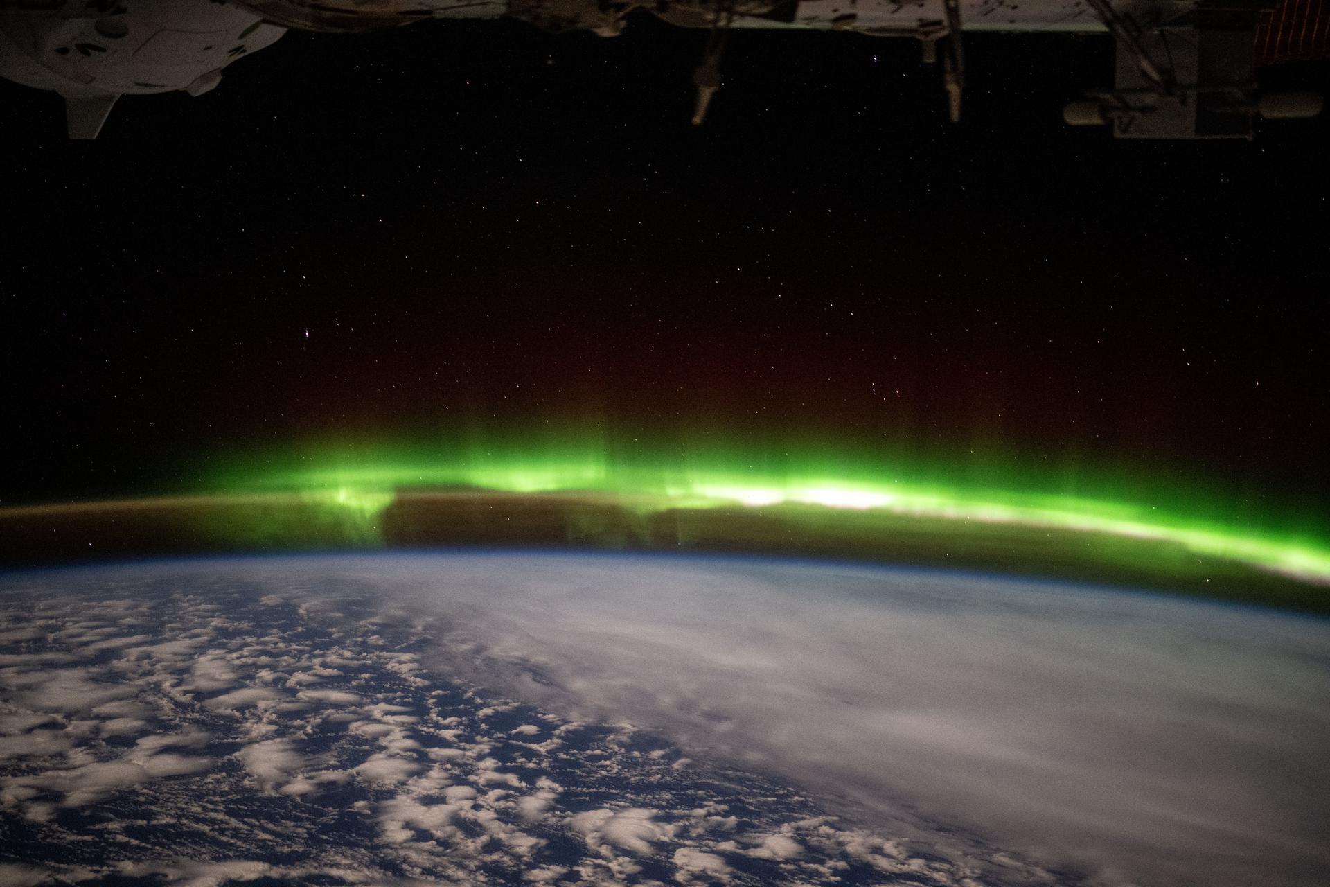 A bright green aurora australis streams above Earth's horizon blanketing the atmospheric glow in this photograph from the International Space Station as it orbited 269 miles above a cloudy southern Indian Ocean midway between South Africa and Antarctica.