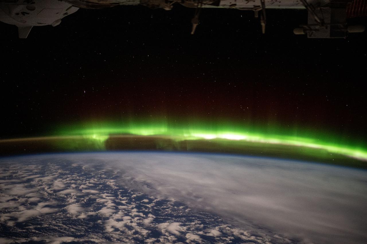 iss073e0246858 (June 9, 2025) --- A bright green aurora australis streams above Earth's horizon blanketing the atmospheric glow in this photograph from the International Space Station as it orbited 269 miles above a cloudy southern Indian Ocean midway between South Africa and Antarctica.