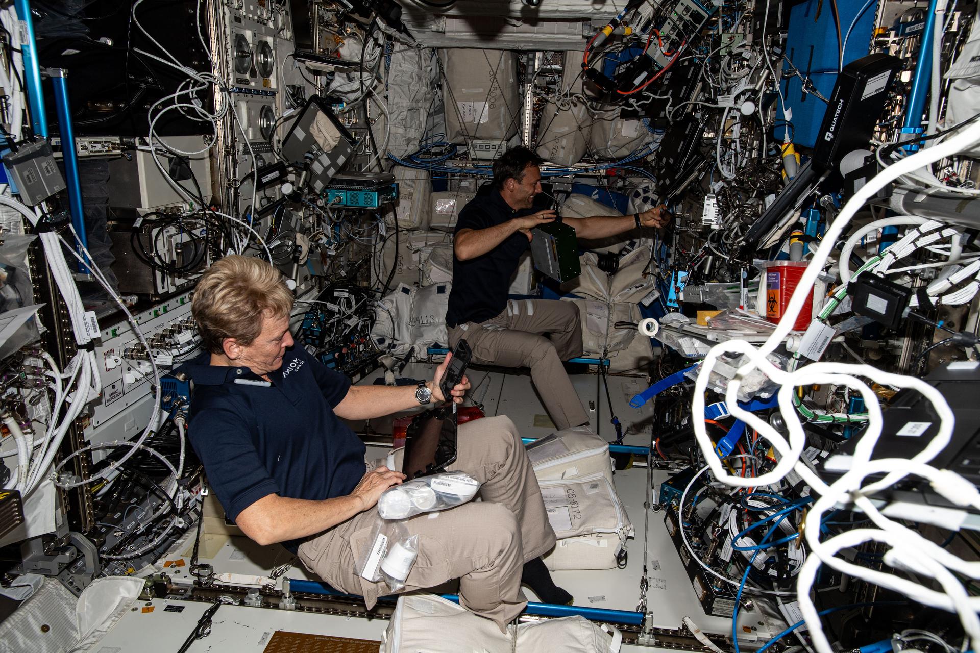 Axiom Mission 4 crew members Peggy Whitson (foreground) from Axiom Space and Sławosz Uznański-Wiśniewski from ESA (European Space Agency) work inside the International Space Station's Columbus laboratory module. The private astronaut duo swapped research hardware supporting the Space Volcanic Algae biotechnology study and the Experiment Cube #25 data processing and algorithm investigation.