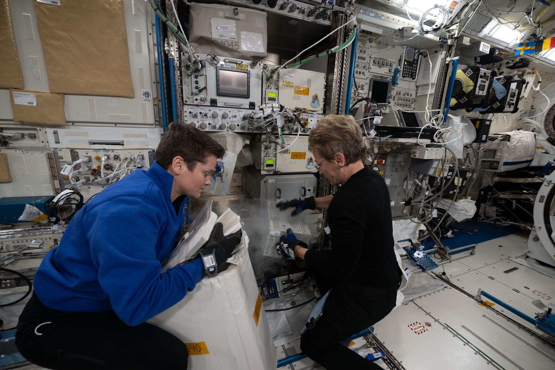 (From left) Expedition 73 Flight Engineer Anne McClain of NASA helps Axiom Mission 4 Commander Peggy Whitson from Axiom Space pack frozen research samples aboard the International Space Station before loading them inside the SpaceX Dragon crew spacecraft for return to Earth.