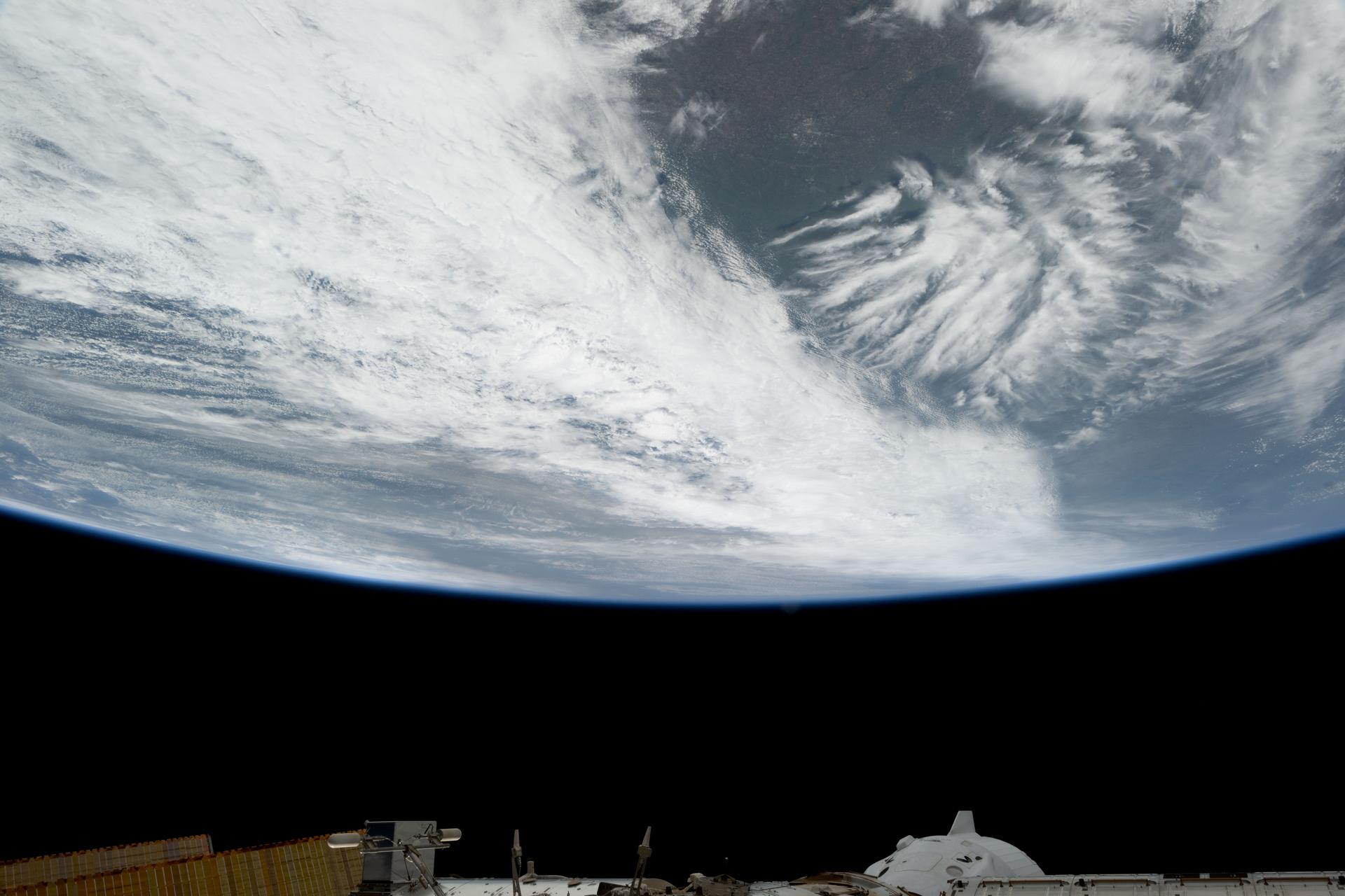 Wichita, Kansas, is pictured in the center of a wide open gap surrounded by clouds covering the midwestern United States in this photograph from the International Space Station as it orbited 261 miles above. At bottom right, a portion of the SpaceX Dragon crew spacecraft is seen docked to the orbital outpost's forward port on the Harmony module.