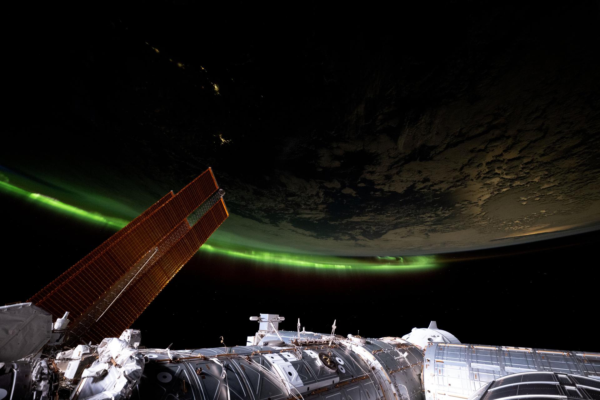 An aurora streams across Earth's horizon in this photograph from the International Space Station as it orbited 266 miles above the Bass Strait off the coast of southeast Australia. At left, a set of the orbital outpost's main solar arrays extend across the frame. At bottom, a portion of the station's U.S. segment is illuminated including the SpaceX Dragon crew spacecraft docked to the Harmony module's forward port in this photograph taken from the cupola at approximately 6:56 p.m. local time.