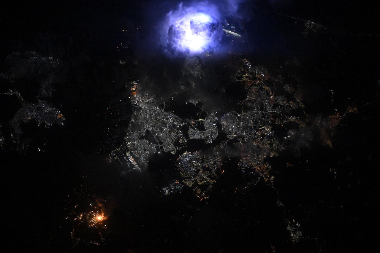 iss073e0300048 (June 15, 2025) --- Lightning (top center) is captured striking and illuminating the clouds during a storm over the Southeast Asian city-state of Singapore separated from the Malaysian city of Johor Bahru by the Johor Strait. Singapore's population is just over 6 million while Johor Bahru's is nearly 860,000. The International Space Station was orbiting 259 miles above the South China Sea at approximately 3:18 a.m. local time when this photograph was taken.