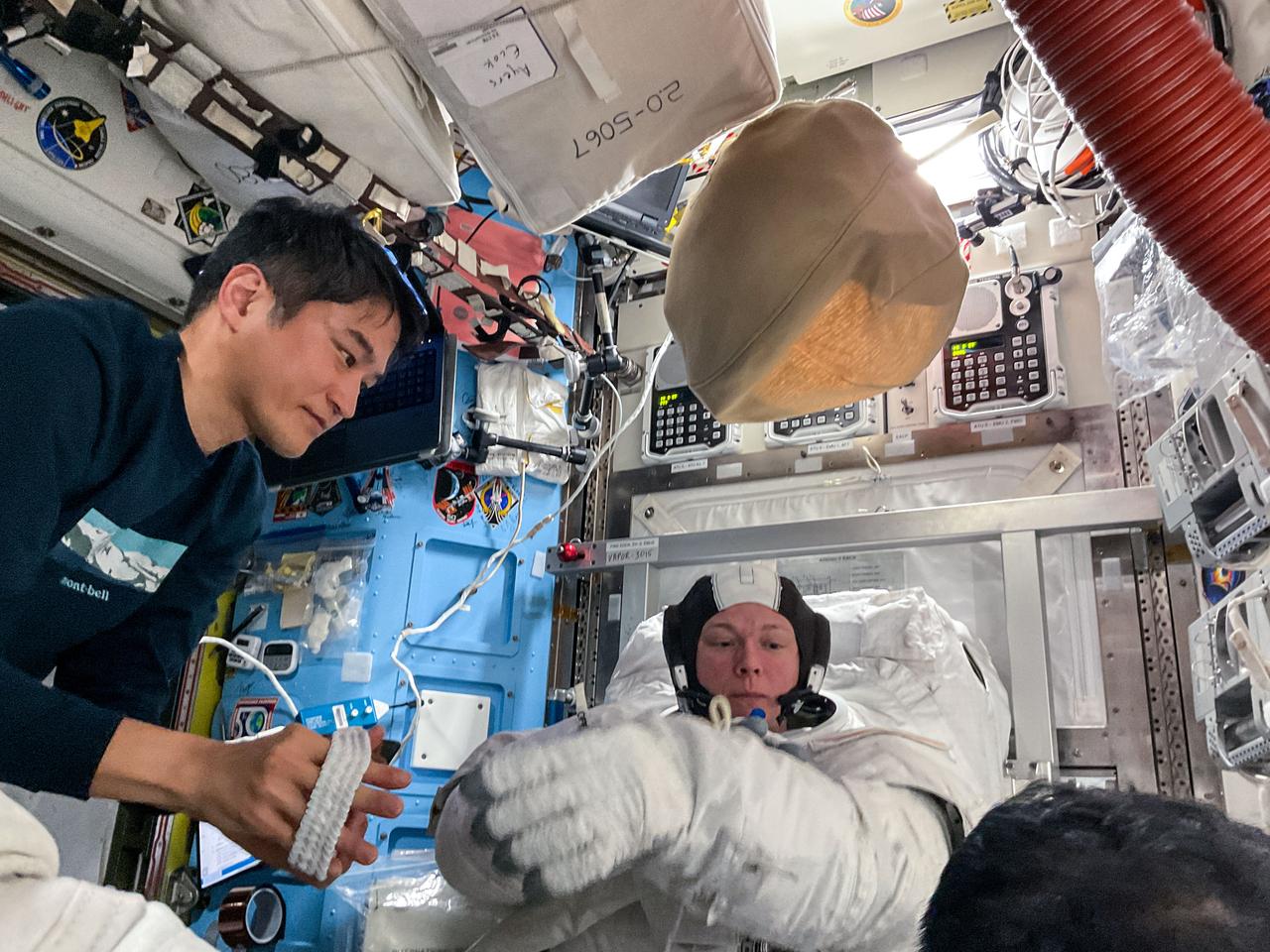 iss073e0379898 (May 1, 2025) --- Expedition 73 Commander Takuya Onishi from JAXA (Japan Aerospace Exploration Agency) assists Flight Engineer Nichole Ayers from NASA as she tries on a spacesuit and tests its components during a fit check inside the International Space Station's Quest airlock.