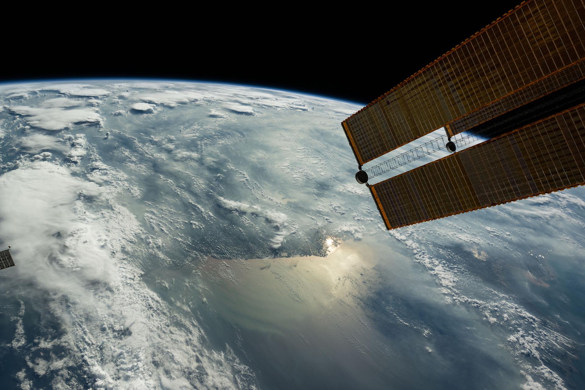 The sun's glint beams off the Yellow Sea coast of Jiangsu Province, China, in this photograph taken from the International Space Station as it orbited 260 miles above. In the right foreground, a set of the station's main solar arrays extends into the frame.