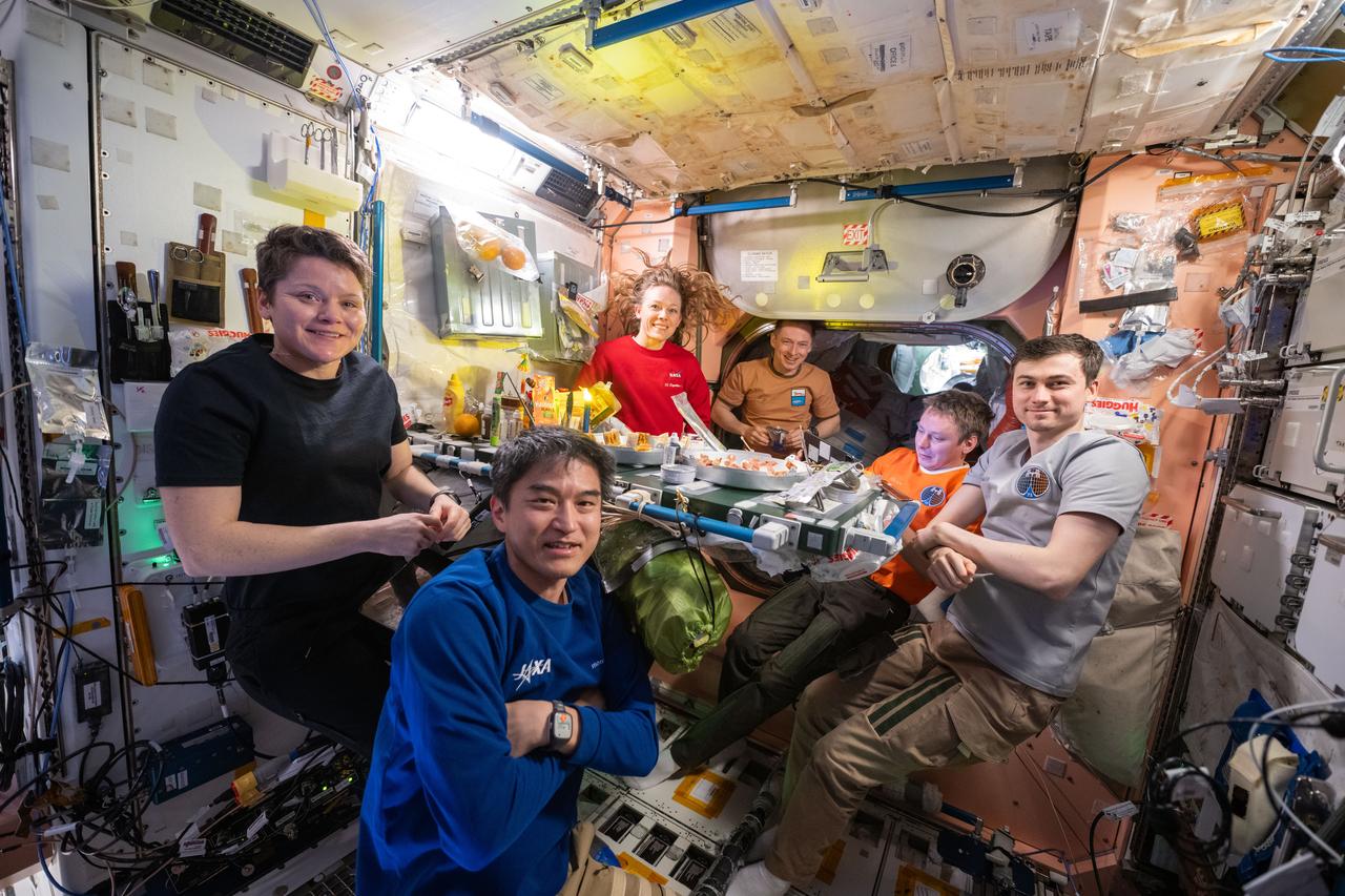 iss073e0417307 (July 25, 2025) --- Six of seven Expedition 73 crew members pose for a portrait during dinnertime at the galley inside the International Space Station's Unity module. Clockwise from bottom are, JAXA (Japan Aerospace Exploration Agency) astronaut Takuya Onishi, NASA astronauts Anne McClain and Nichole Ayers, and Roscosmos cosmonauts Sergey Ryzhikov, Kirill Peskov, and Alexey Zubritsky.