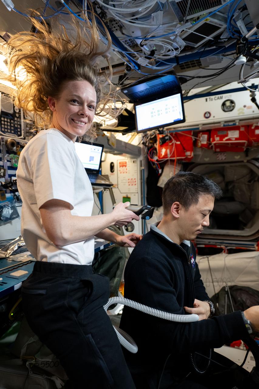 iss073e0422025 (July 27, 2025) --- NASA astronauts Nichole Ayers and Jonny Kim, both Expedition 73 Flight Engineers, are pictured inside the International Space Station's Harmony module. Ayers trims Kim's hair as a suction hose collects loose hairs to protect the station's atmosphere.