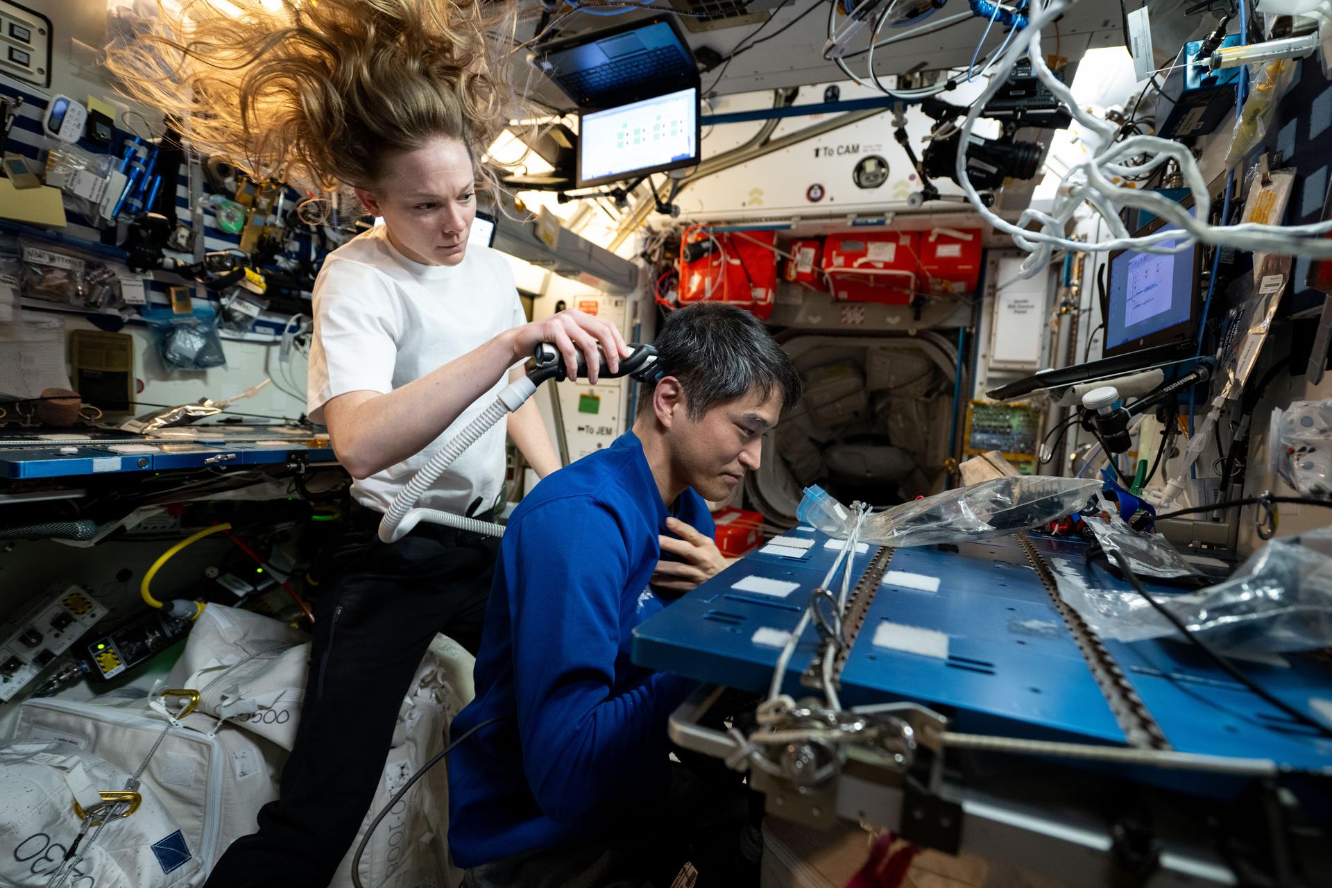 Expedition 73 Flight Engineer Nichole Ayers of NASA gives International Space Station Commander Takuya Onishi of JAXA (Japan Aerospace Exploration Agency) a haircut as a suction hose collects loose hairs to protect the station's atmosphere.