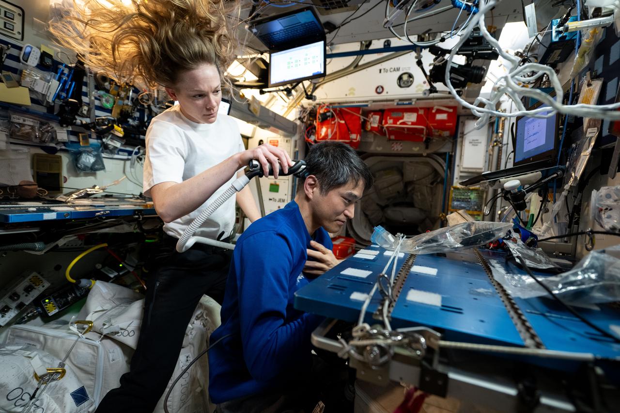 iss073e0422042 (July 27, 2025) --- Expedition 73 Flight Engineer Nichole Ayers of NASA gives International Space Station Commander Takuya Onishi of JAXA (Japan Aerospace Exploration Agency) a haircut as a suction hose collects loose hairs to protect the station's atmosphere.