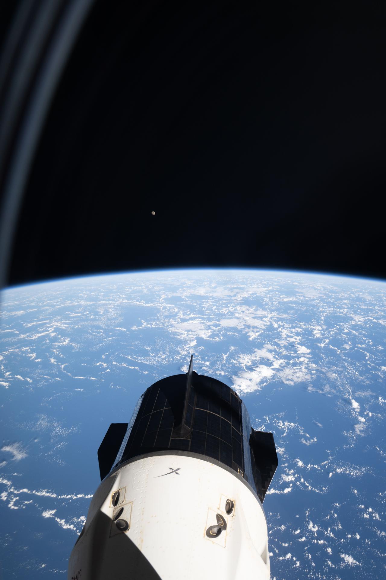 The SpaceX Dragon crew spacecraft that ferried NASA’s Crew-10 mission to the International Space Station is seen docked to the forward port of the Harmony module, as photographed from NASA’s SpaceX Crew-11 Dragon spacecraft attached to Harmony’s space-facing port. Just above Earth’s horizon at center left, a tiny white dot marks the Waxing Gibbous Moon. This image was captured as the orbital outpost soared 259 miles above the Atlantic Ocean.