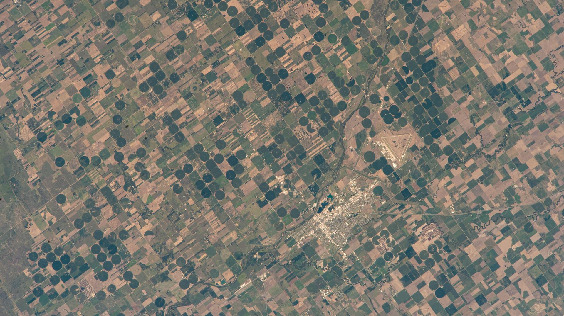 Great Bend, Kansas, primarily an agricultural town and located at the point where the Arkansas River course shifts, is pictured from the International Space Station as it orbited 261 miles above the Sunflower State. The triangular Great Bend Municipal Airport, once used as a base for the B-29 Superfortress during WWII and now used for general aviation, can also be seen.