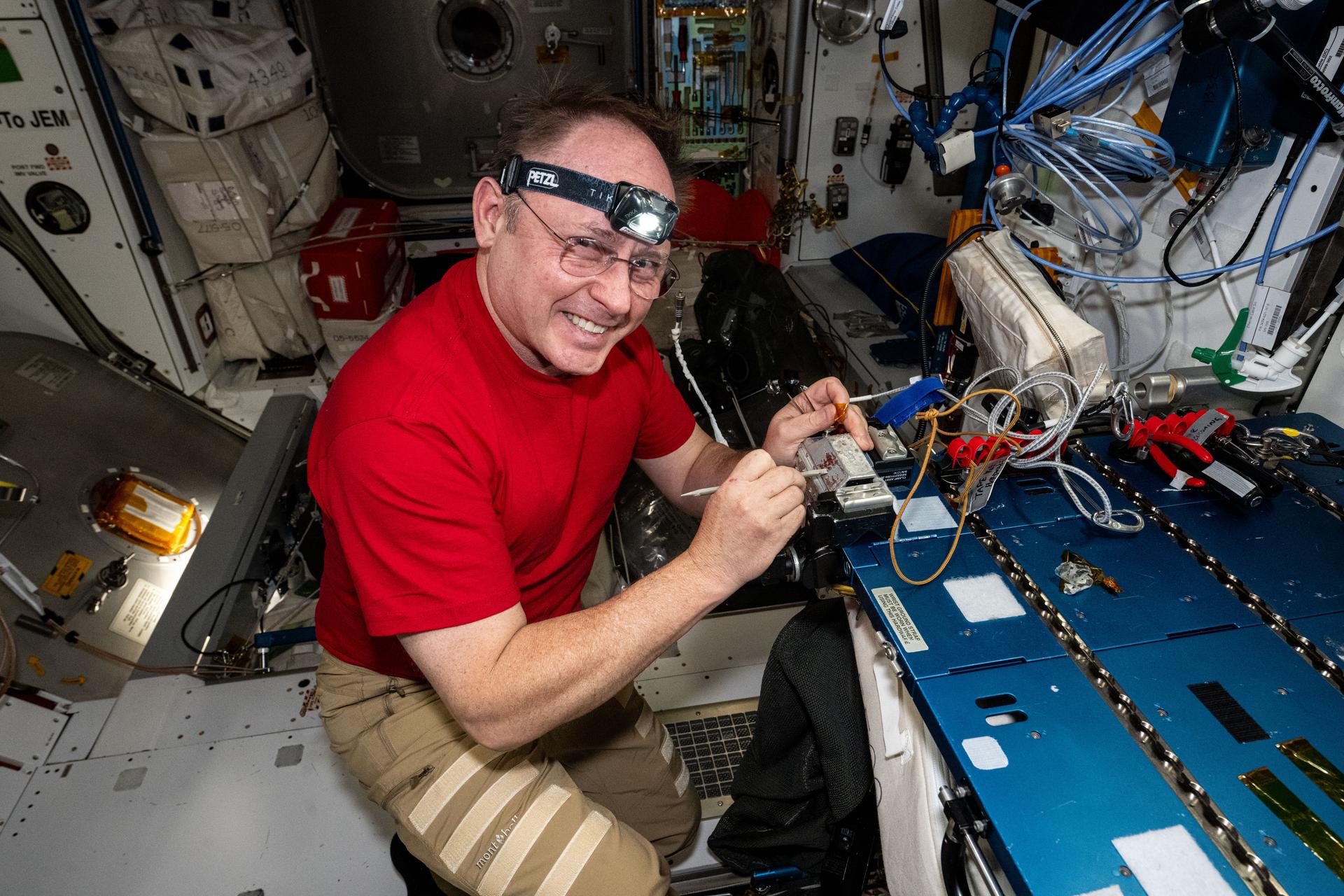 iss073e0510683 (Aug. 18, 2025) --- NASA astronaut and Expedition 73 Flight Engineer Mike Fincke replaces thermal tape on a High Definition Extravehicular Mobility Unit Camera, or HECA. The spacesuit helmet-mounted camera streams real-time, high-definition video of spacewalk activities to mission controllers on the ground, while the thermal tape shields the HECA from the harsh environment of space.