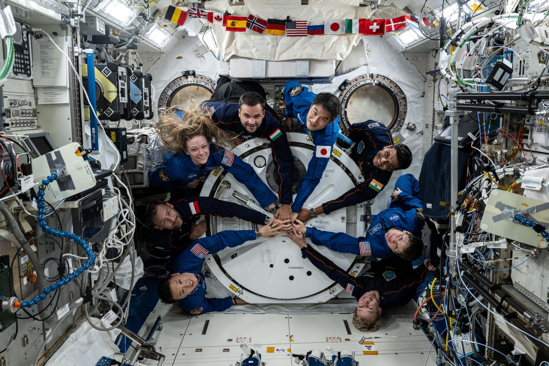 Four astronauts representing Expedition 73 and the four-member Axiom Mission 4 (Ax-4) crew gather for a fun portrait clasping hands and surrounding the Kibo laboratory module's airlock. Clockwise from bottom left are, Expedition 73 Flight Engineer Jonny Kim of NASA, Ax-4 Mission Specialist Sławosz Uznański-Wiśniewski of ESA (European Space Agency), Expedition 73 Flight Engineer Nichole Ayers of NASA, Ax-4 Mission Specialist Tibor Kapu from Hungary, Expedition 73 Commander Takuya Onishi of JAXA (Japan Aerospace Exploration Agency), Ax-4 Pilot Shubhanshu Shukla of ISRO (Indian Space Research Organization), Expedition 73 Flight Engineer Anne McClain of NASA, and Ax-4 Commander Peggy Whitson of Axiom Space.