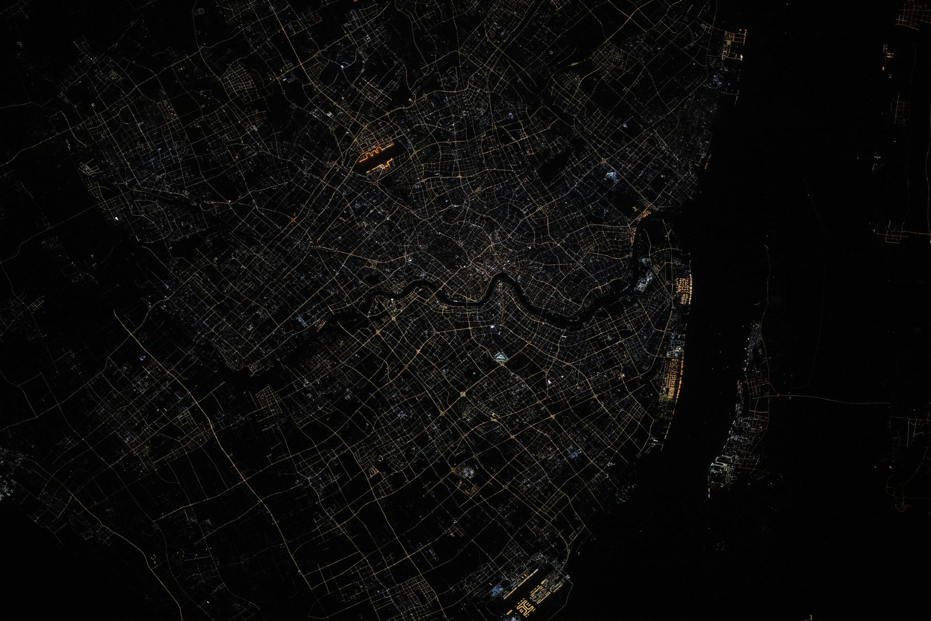 Shanghai, China, situated on the Yangtze River where it meets the East China Sea, is pictured at approximately 1:32 a.m. local time from the International Space Station as it orbited 261 miles above the nation's eastern coastline. Visible landmarks include Shanghai Hongqiao International Airport near the top of the frame and Shanghai Pudong International Airport at the bottom. The city's lights appear dimmer from orbit due to the widespread use of modern, downward-facing, energy-efficient lighting that reduces light pollution.