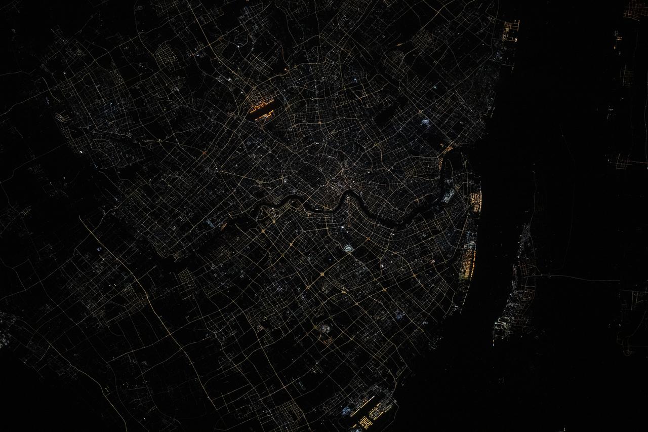 iss073e0515603 (Aug. 24, 2025) --- Shanghai, China, situated on the Yangtze River where it meets the East China Sea, is pictured at approximately 1:32 a.m. local time from the International Space Station as it orbited 261 miles above the nation's eastern coastline. Visible landmarks include Shanghai Hongqiao International Airport near the top of the frame and Shanghai Pudong International Airport at the bottom. The city's lights appear dimmer from orbit due to the widespread use of modern, downward-facing, energy-efficient lighting that reduces light pollution. Credit: JAXA (Japan Aerospace Exploration Agency)