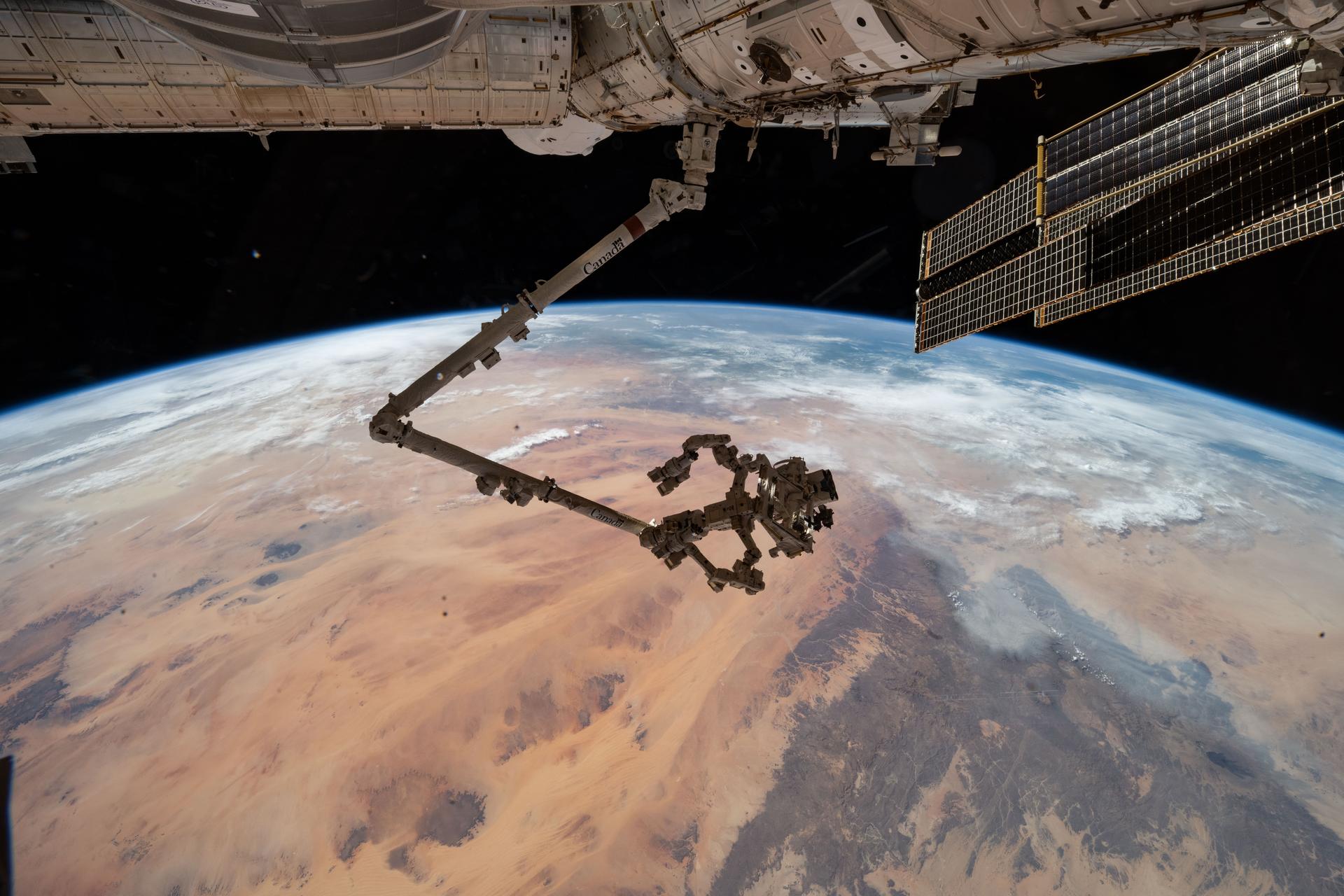 The International Space Station's 57.7-foot-long robotic arm, Canadarm2, with its fine-tuned robotic hand, Dextre, attached is pictured extending from the International Space Station's Harmony module. The orbital outpost was soaring 260 miles above the Saharan Desert in Libya at the time of this photograph.