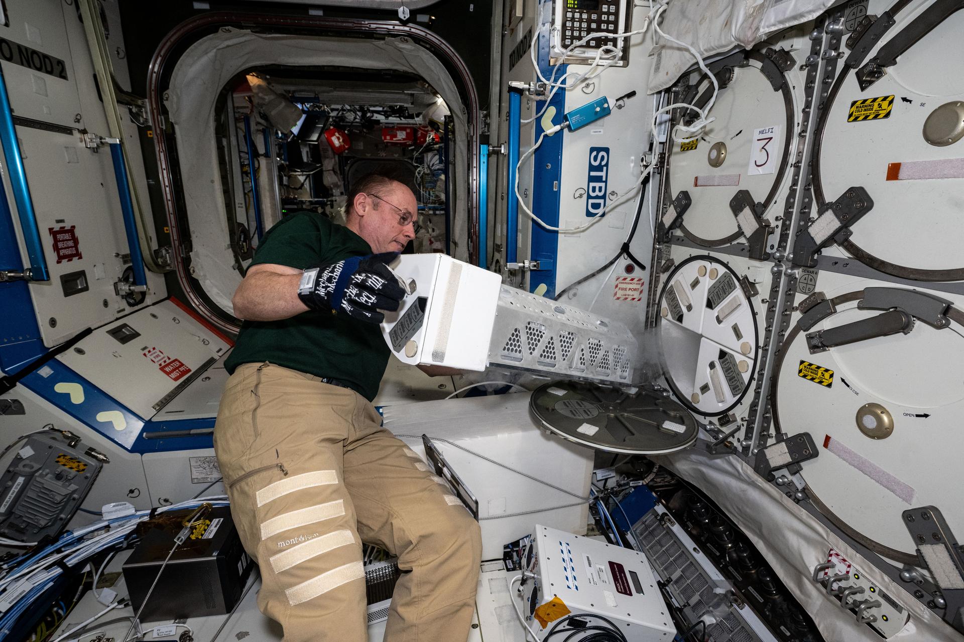 NASA astronaut and Expedition 73 Flight Engineer Mike Fincke inserts a cryogenic storage unit, called a dewar, containing blood samples collected from a crew member into a science freezer for preservation and later analysis. The Minus Eighty-Degree Laboratory Freezer for International Space Station, or MELFI, is a research freezer that maintains experiment samples at ultra-cold temperatures in microgravity.
