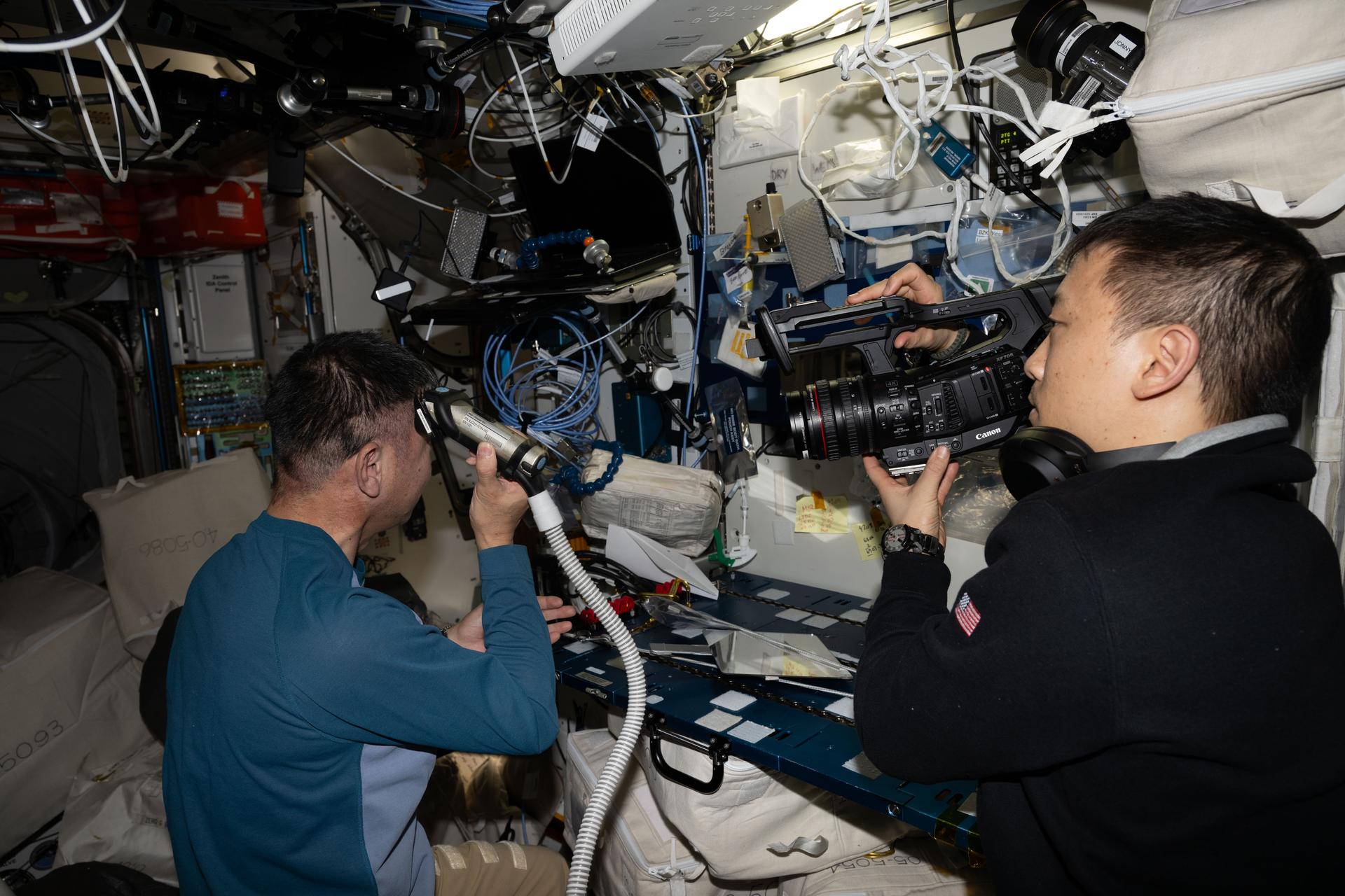 Astronaut Kimiya Yui of JAXA (Japan Aerospace Exploration Agency) trims his own hair aboard the International Space Station as NASA astronaut Jonny Kim films the crew activities. Attached to the electric razor is a vacuum that collects the loose hair safeguarding the station's atmosphere in the microgravity environment.