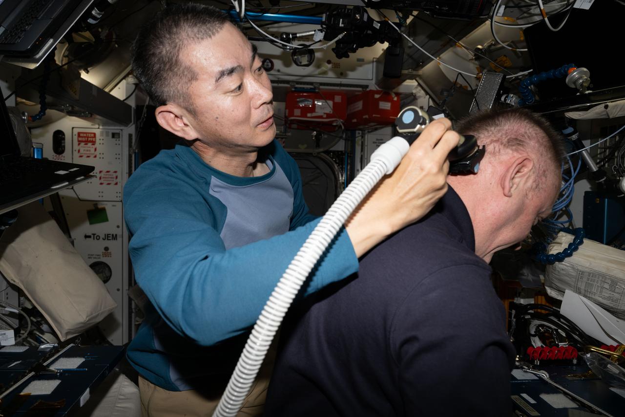 iss073e0602995 (Aug. 30, 2025) --- JAXA (Japan Aerospace Exploration Agency) astronaut Kimiya Yui trims NASA astronaut Mike Fincke's hair aboard the International Space Station. Attached to the electric razor is a vacuum that collects the loose hair safeguarding the station's atmosphere in the microgravity environment.