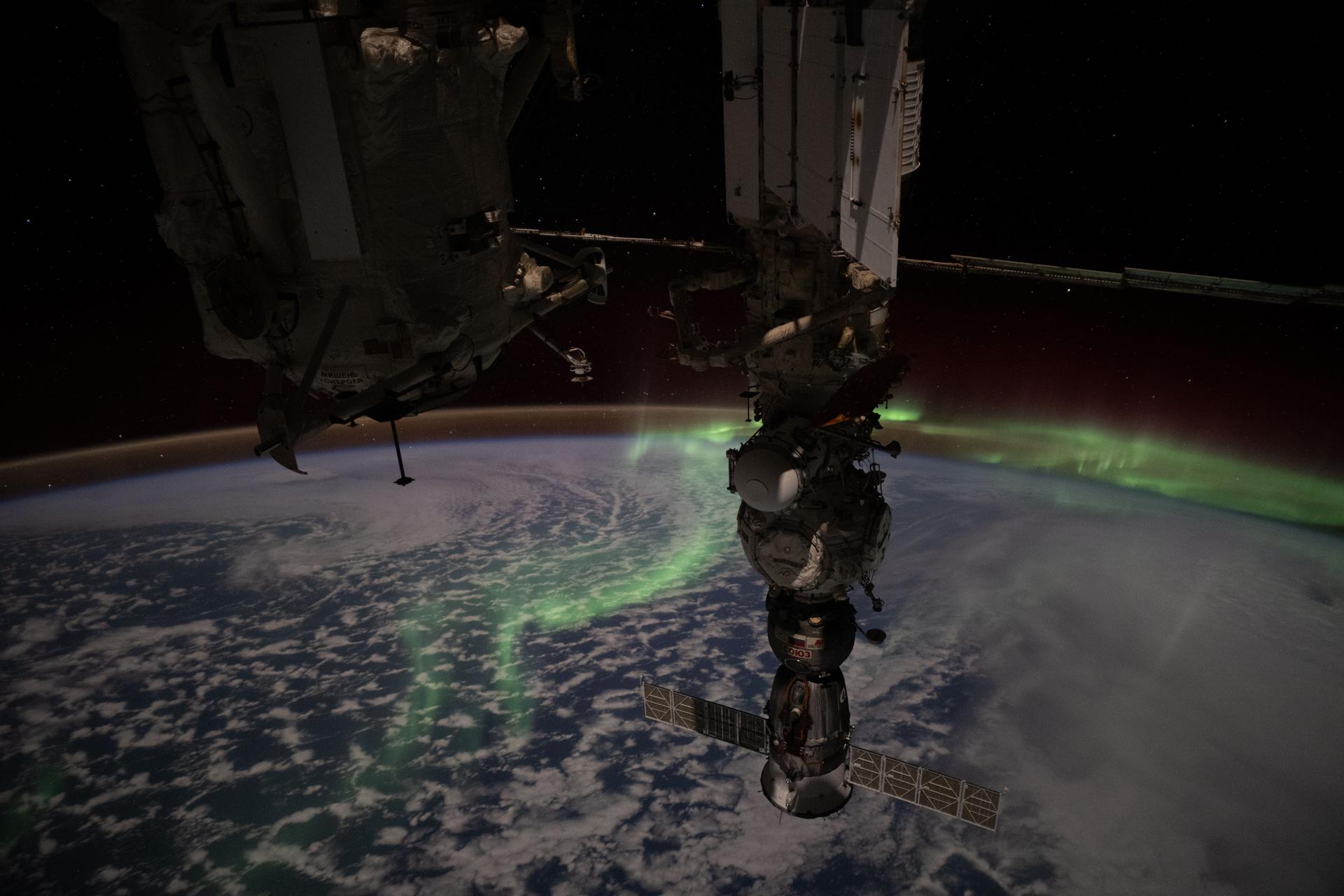 The aurora australis streams above the Earth and into the atmospheric glow in this photograph taken from the International Space Station as it orbited 269 miles above the Indian Ocean midway between Australia and Antarctica at approximately 2:51 a.m. local time. Portions of the orbital outpost's Roscosmos segment are visible in the foreground, including (from left) the Rassvet module and the Soyuz MS-27 crew spacecraft docked to the Prichal module which is itself attached to the Nauka science module.