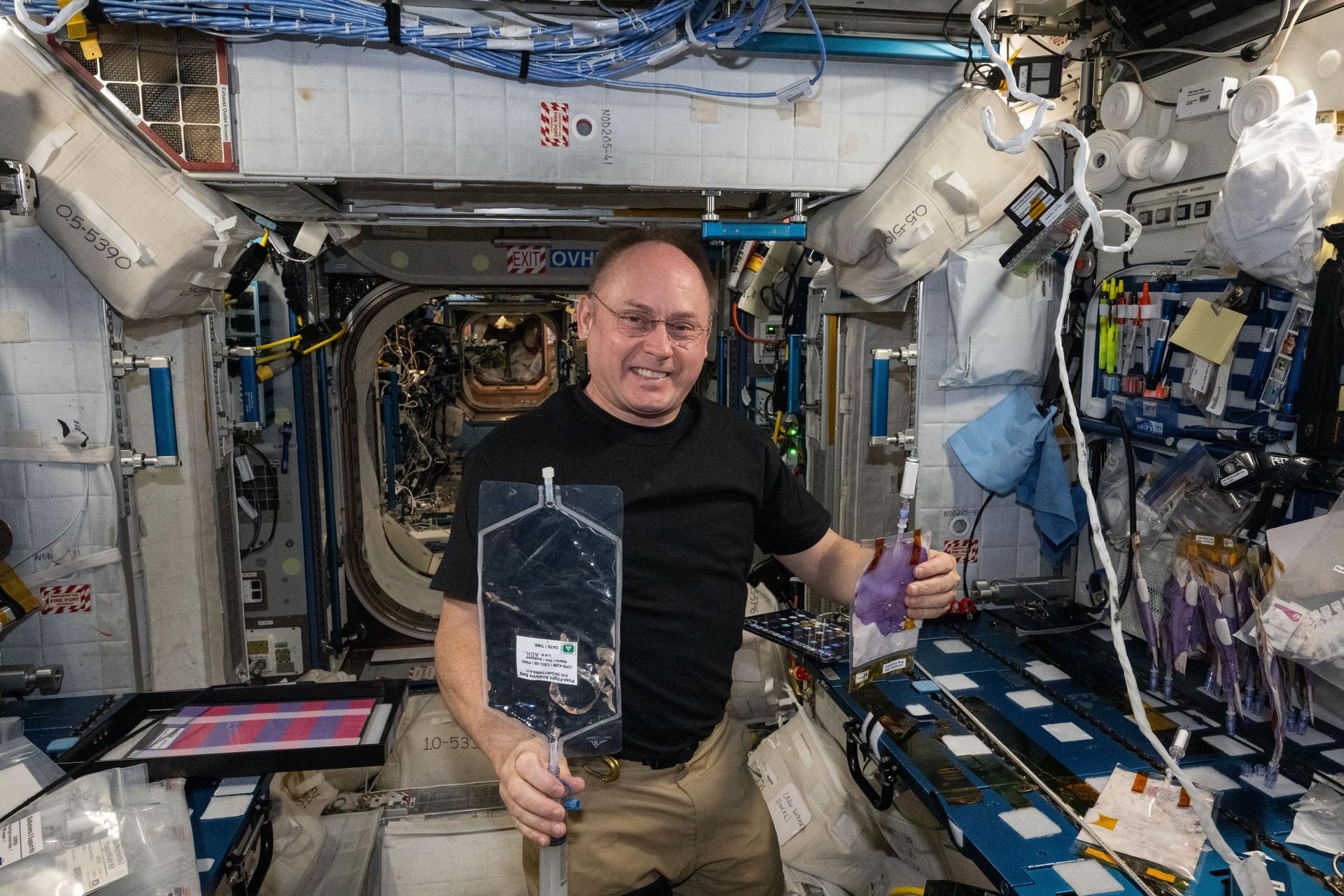 NASA astronaut and Expedition 73 Flight Engineer Mike Fincke shows off production packs containing research samples for the BioNutrients-3 investigation. The biotechnology study explores ways to produce vitamins and nutrients on spacecraft helping supply adequate nutrition for long-term space missions. Fincke treated yeast, yogurt, and fermented milk samples then stowed them in a research incubator for later analysis.