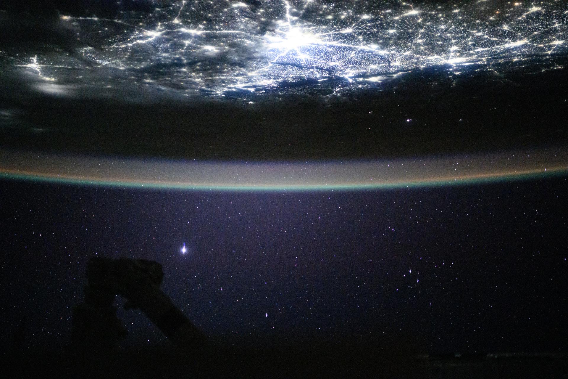 Underneath a starry night sky, the city lights of New Delhi, India, and its surrounding suburbs glitter below Earth's atmospheric glow and at the edge of the Himalayas. This photograph was taken at approximately 2:55 a.m. local time as the International Space Station orbited 260 miles above.