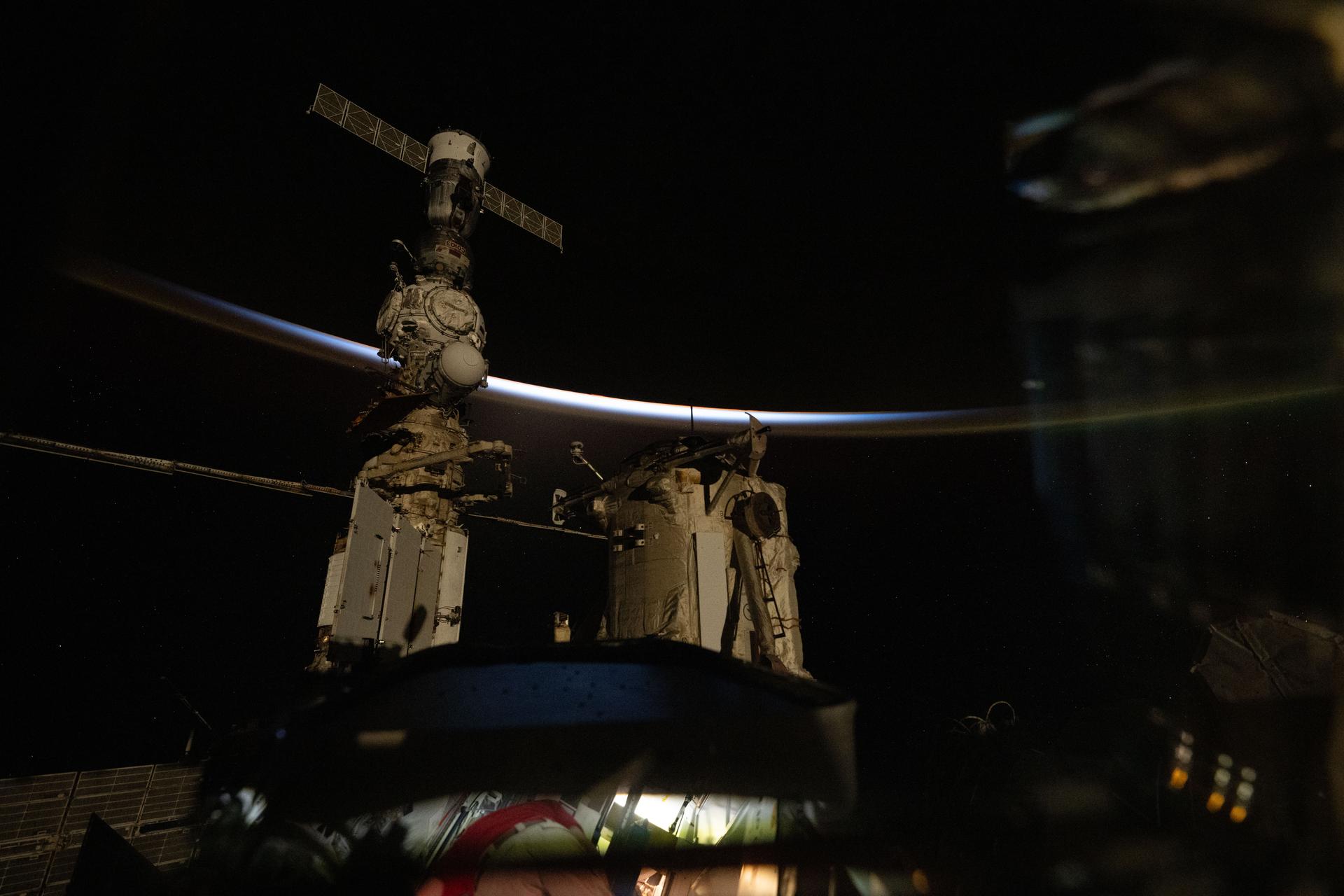 The last rays of an orbital sunset outline Earth's horizon revealing faint orange and blue hues and an atmospheric glow in this photograph from the International Space Station as it orbited 268 miles above the Indian Ocean. In the foreground, is the orbital outpost's Roscosmos segment including the Rassvet module, the Nauka science module, and the Prichal module with the docked Soyuz MS-27 spacecraft.
