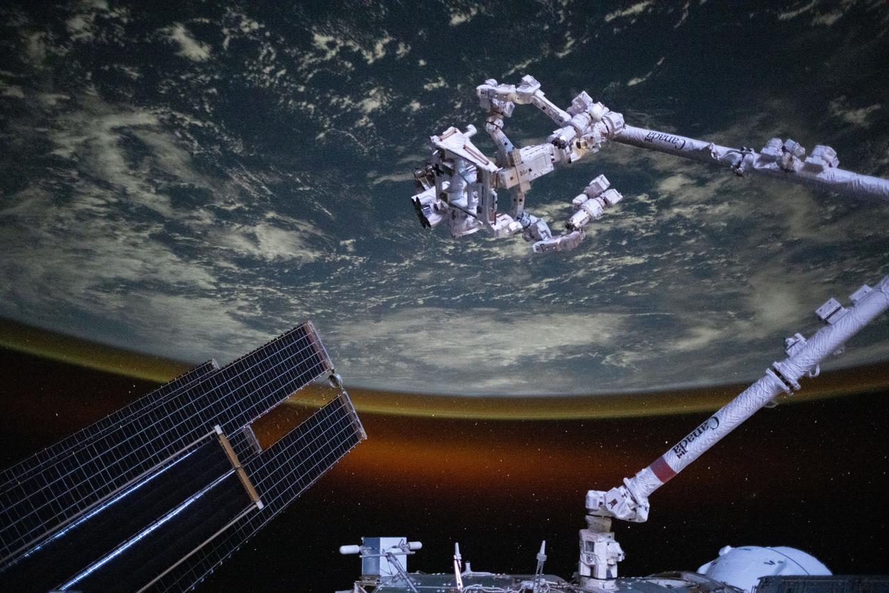 iss073e0695491 (Sept. 1, 2025) --- The Canadarm2 robotic arm with Dextre, its fine-tuned robotic hand attached, is pictured extending from the International Space Station as it orbited 258 miles above the Indian Ocean southwest of the Indonesian island of Sumatra. The Earth's horizon is highlighted by the atmospheric glow with a set of the orbital outpost's main solar arrays and a partially obscured SpaceX Dragon cargo spacecraft in the foreground.