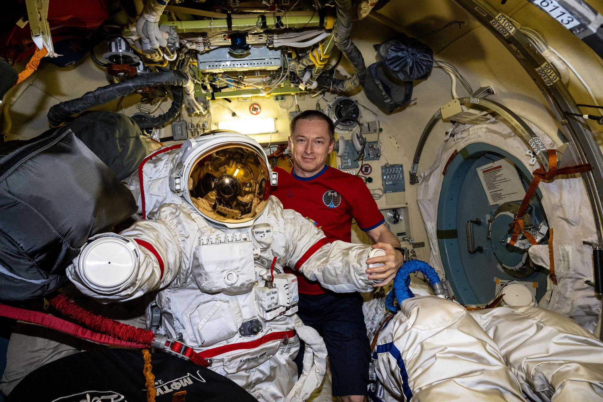 Roscosmos cosmonaut and Expedition 73 Commander Sergey Ryzhikov smiles for a portrait while inspecting an Orlan spacesuit inside the International Space Station's Poisk module.