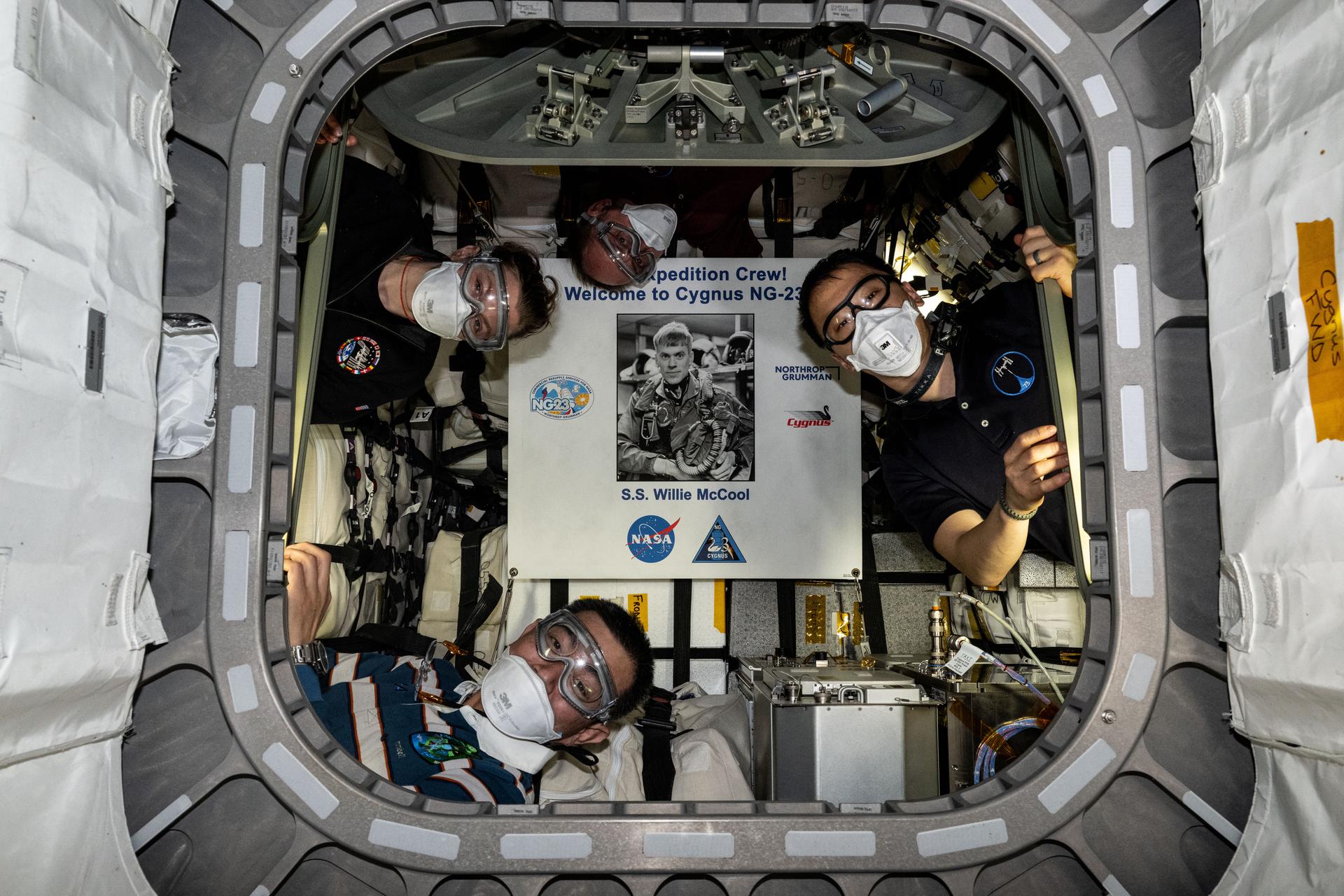 Pictured inside the Northrop Grumman Cygnus XL cargo craft are (clockwise from left) Flight Engineers Zena Cardman, Mike Fincke, and Jonny Kim of NASA, and Flight Engineer Kimiya Yui of JAXA (Japan Aerospace Exploration Agency). The four astronauts are wearing personnel protective equipment as is standard protocol to shield their eyes and lungs from potential dust and debris that may have been dislodged during Cygnus launch to the International Space Station. Highlighted at center, is a poster of William “Willie” McCool, in honor of the NASA astronaut who perished in 2003 during the space shuttle Columbia accident and for whom the Cygnus spacecraft is named.